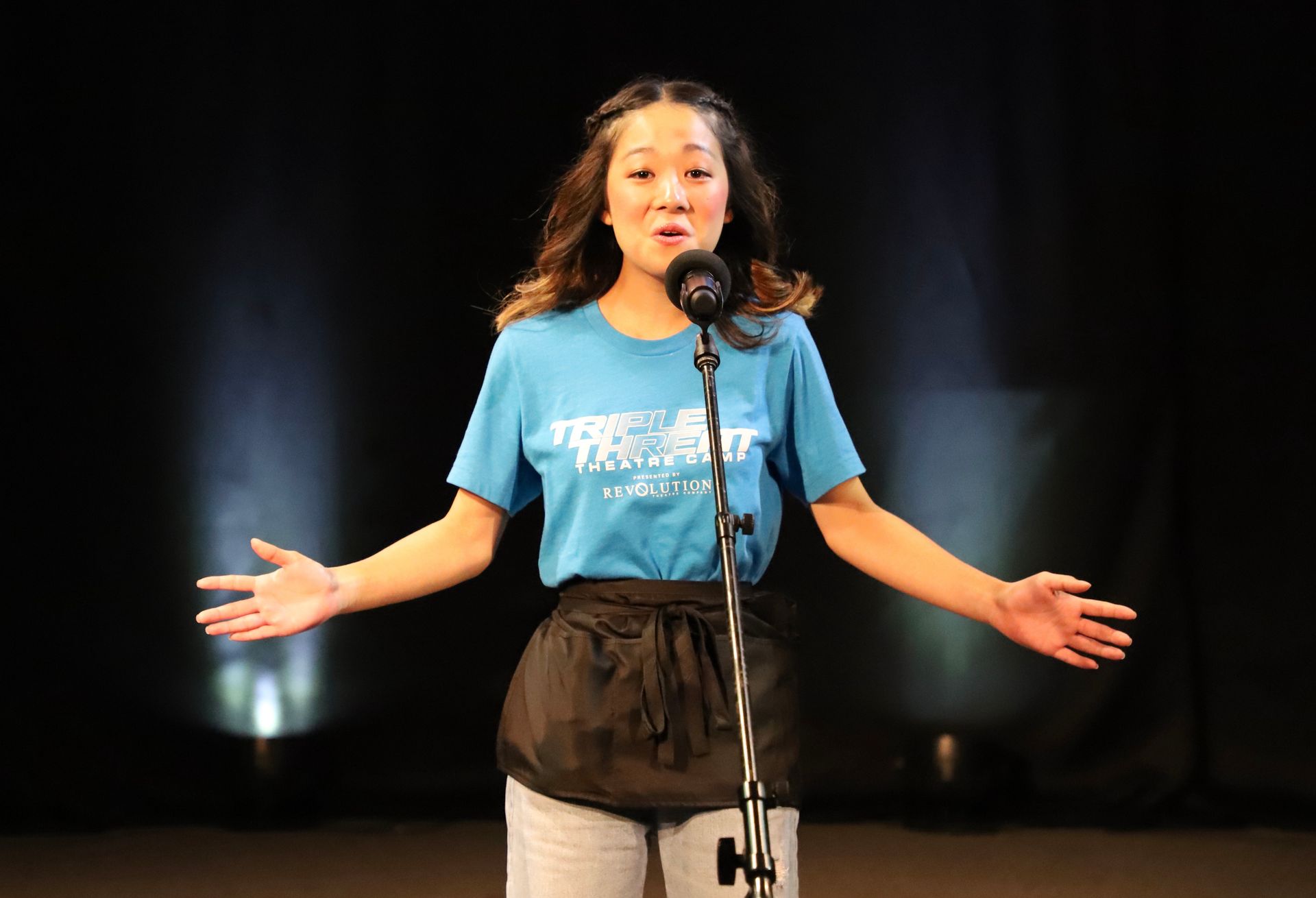 A woman in a blue shirt is singing into a microphone on a stage.