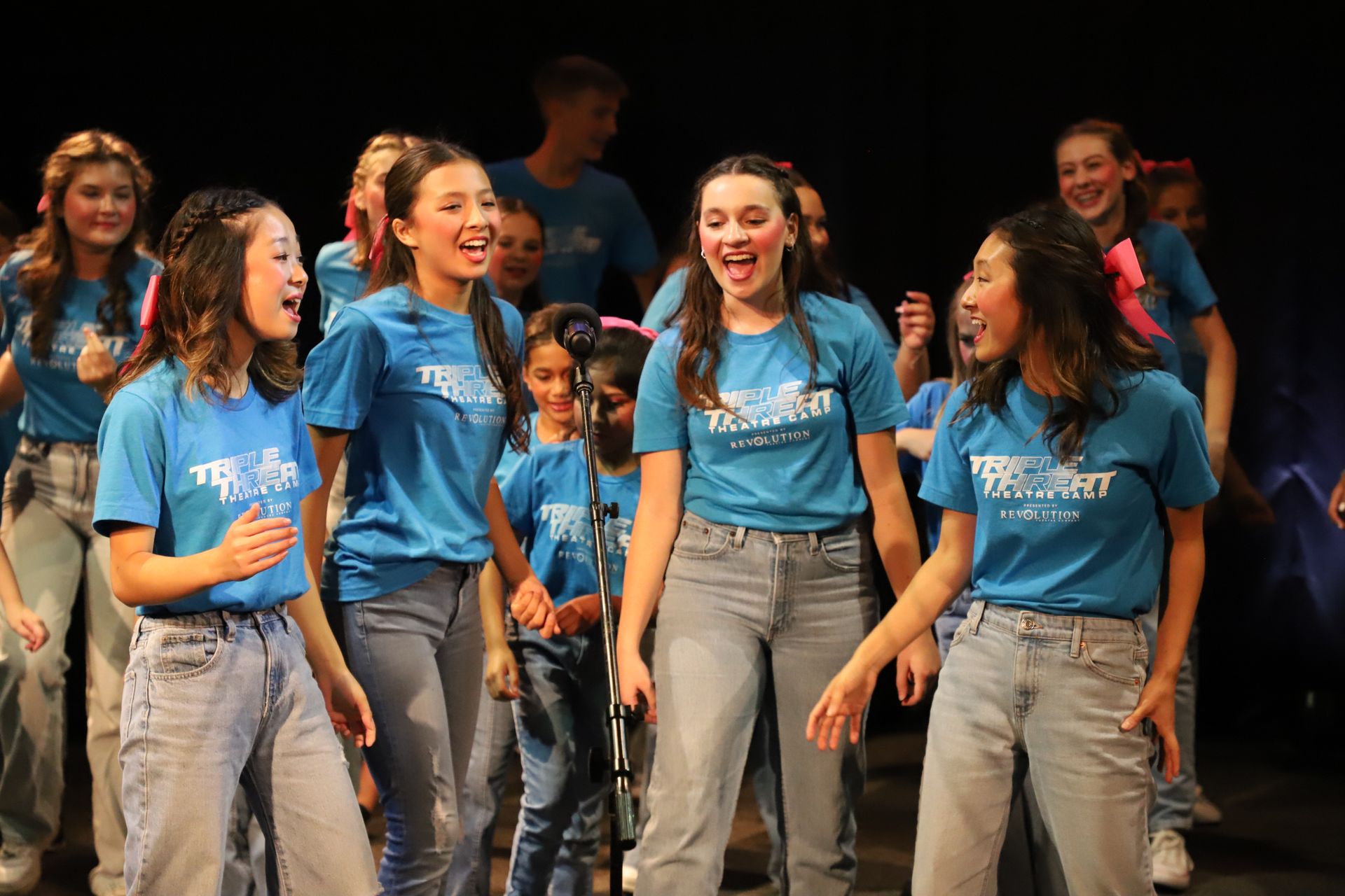 A group of young girls wearing blue shirts and jeans are standing on a stage.