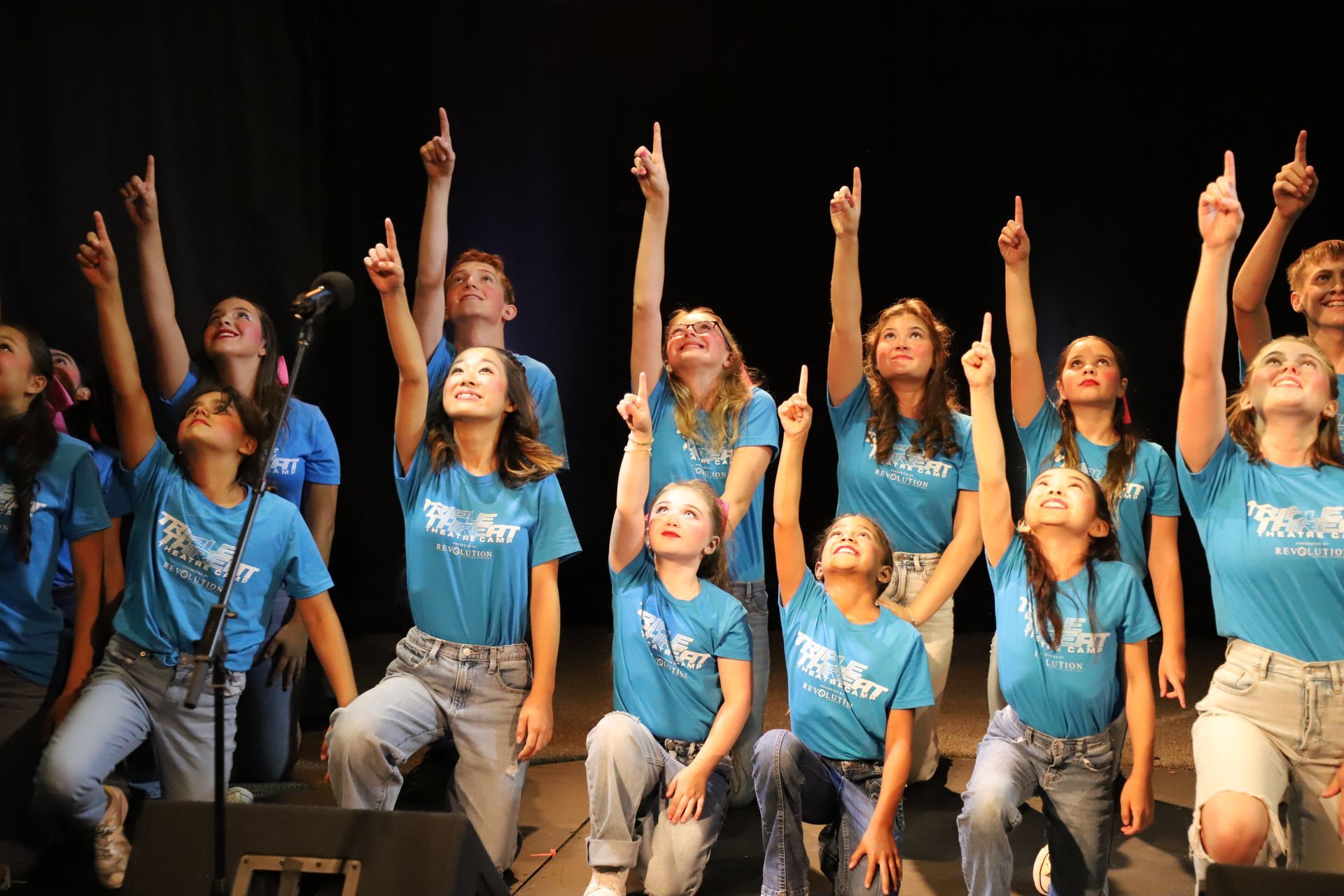 A group of young people in blue shirts are pointing up in the air.