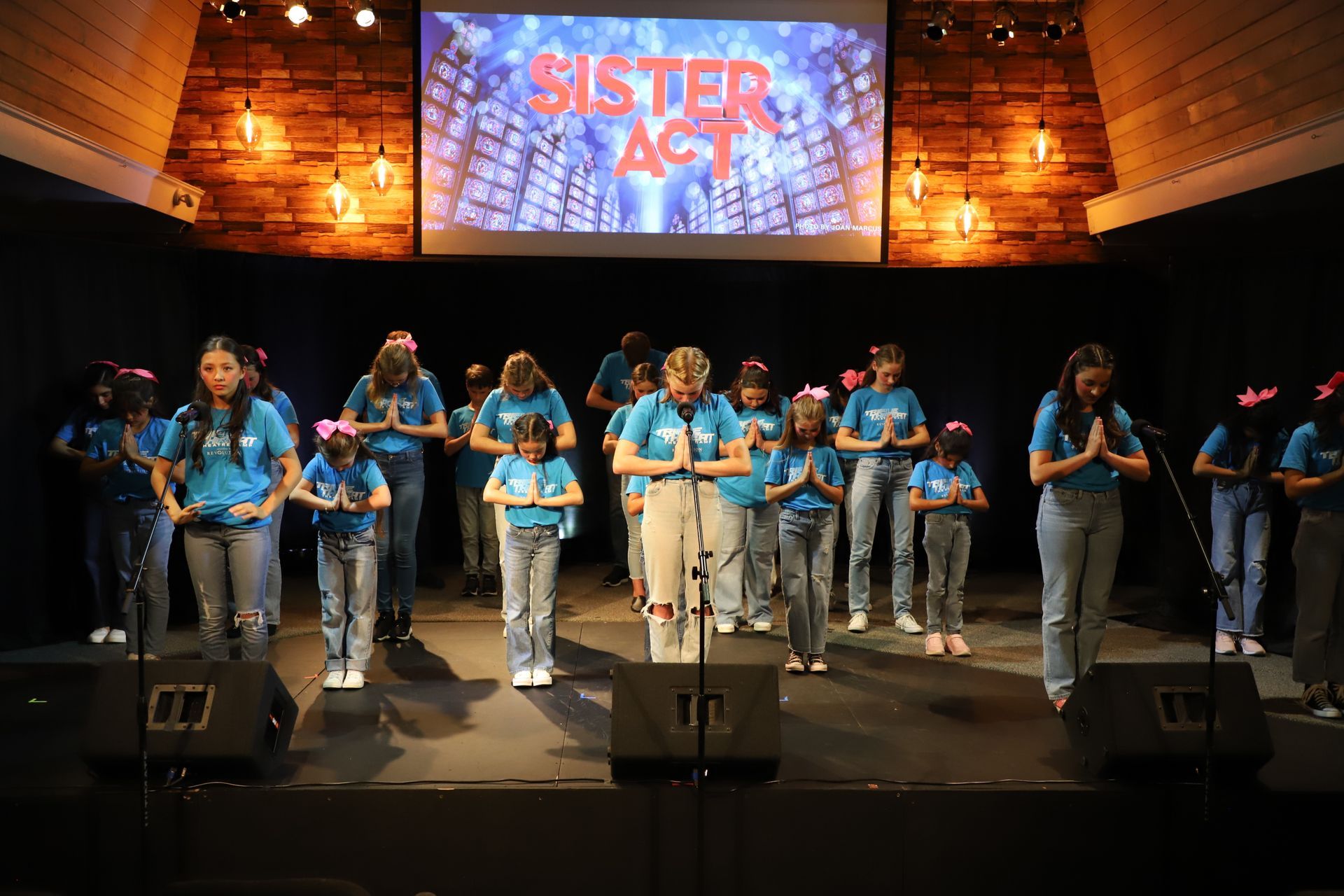 A group of children are singing on a stage in front of a large screen.