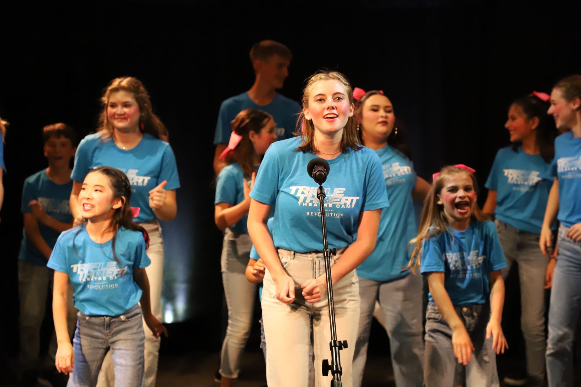 A group of young people are standing in front of a microphone on a stage.