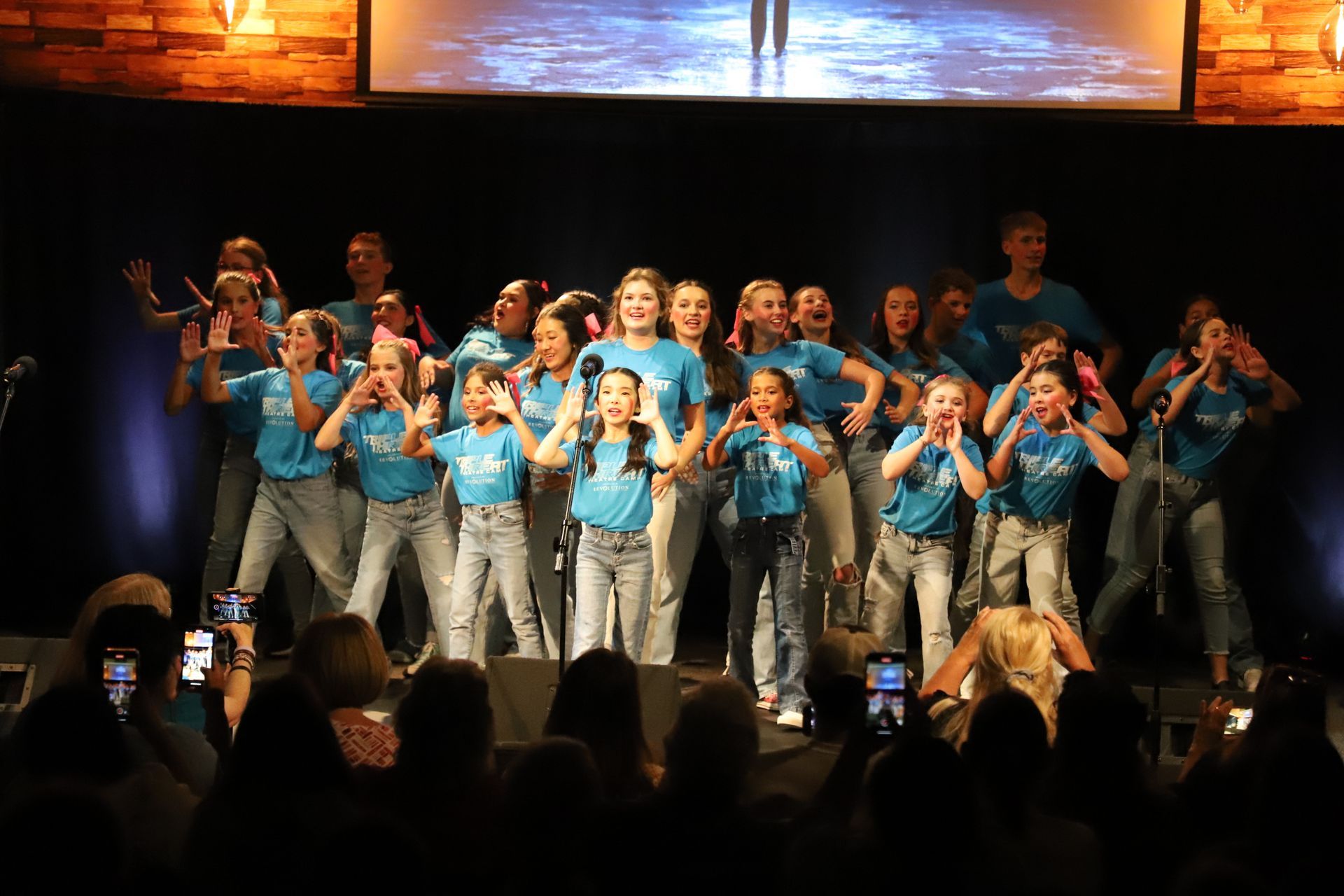 A group of young girls are singing on a stage in front of a crowd.