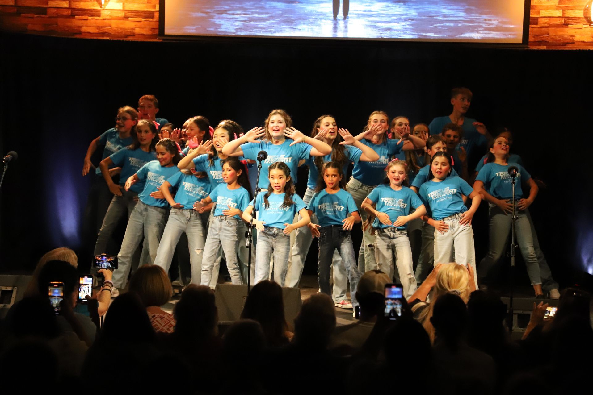 A group of children are standing on a stage singing into microphones.
