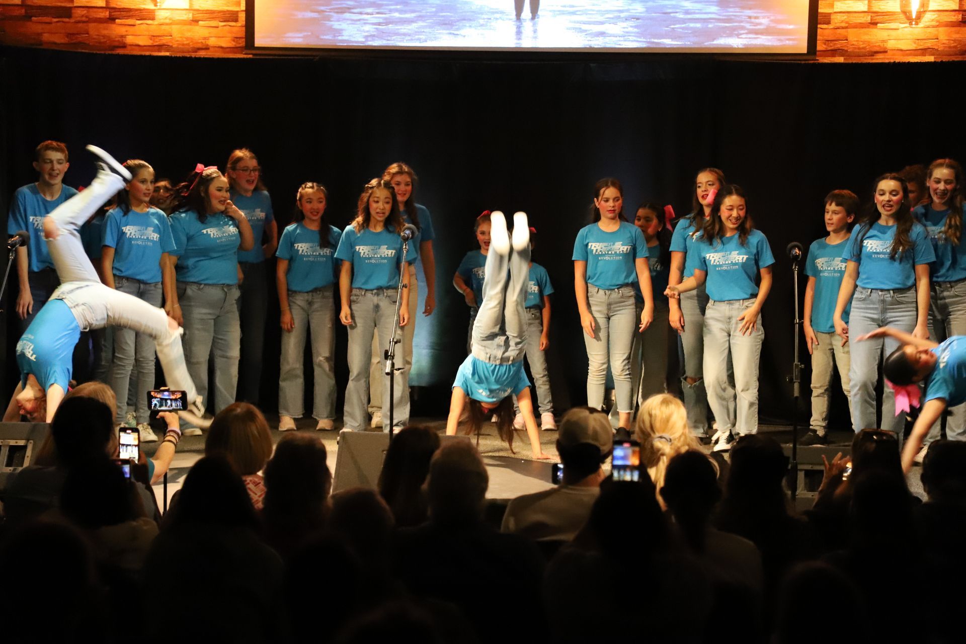 A girl is doing a handstand on a stage in front of a choir.