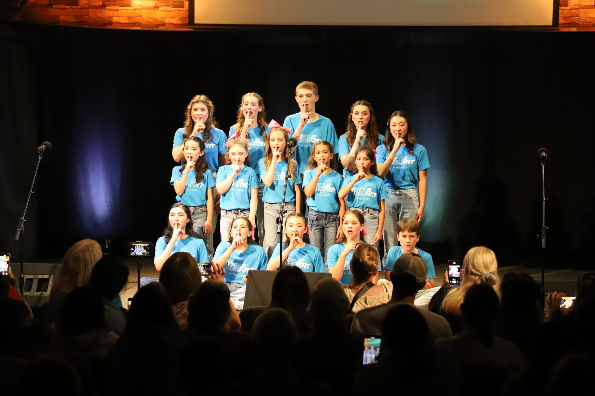 A group of young people are singing on a stage in front of a crowd.