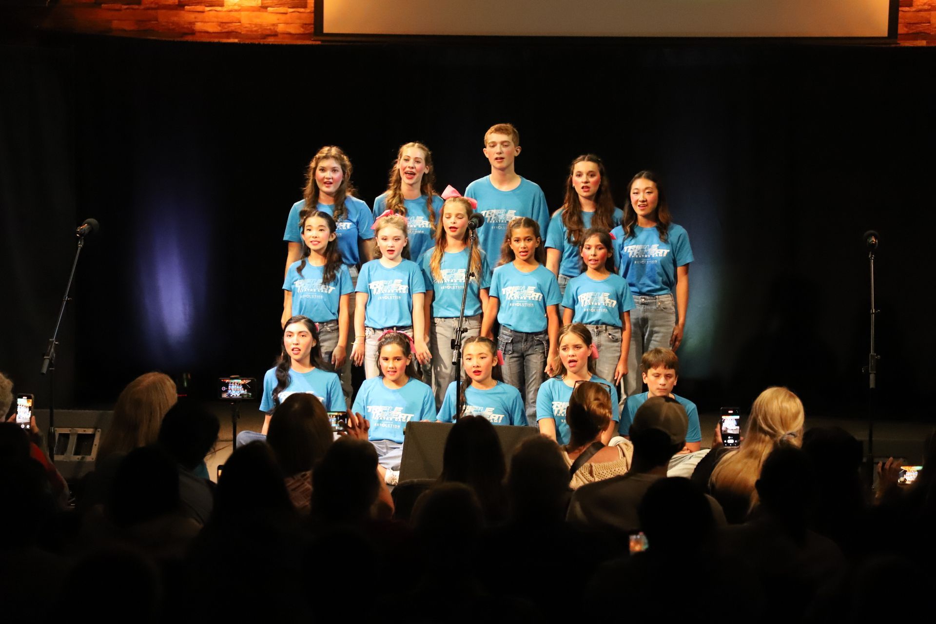 A group of children are singing on a stage in front of a crowd.