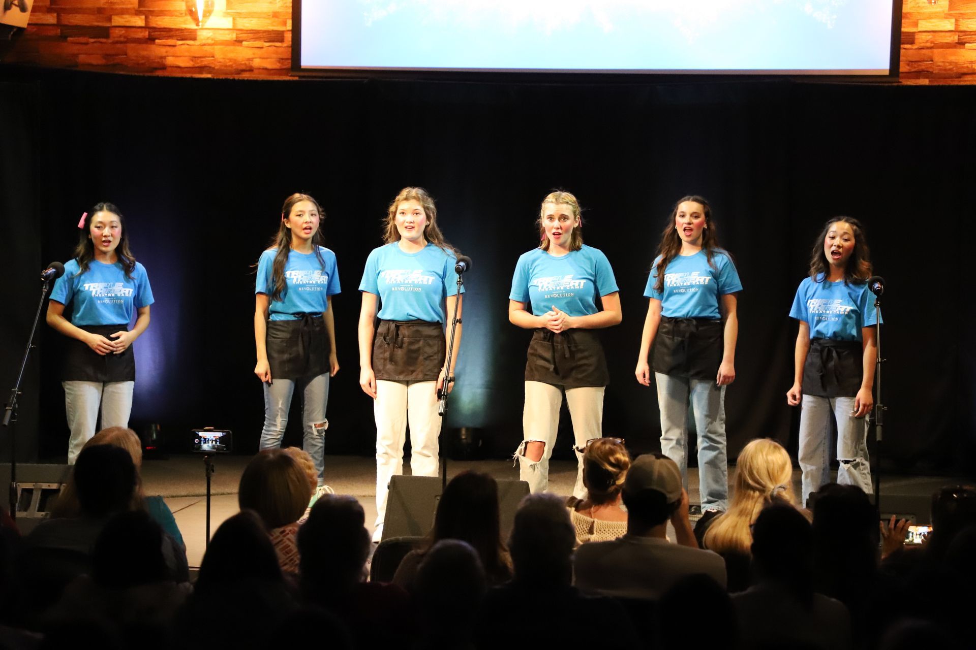 A group of young women are singing on a stage in front of a crowd.