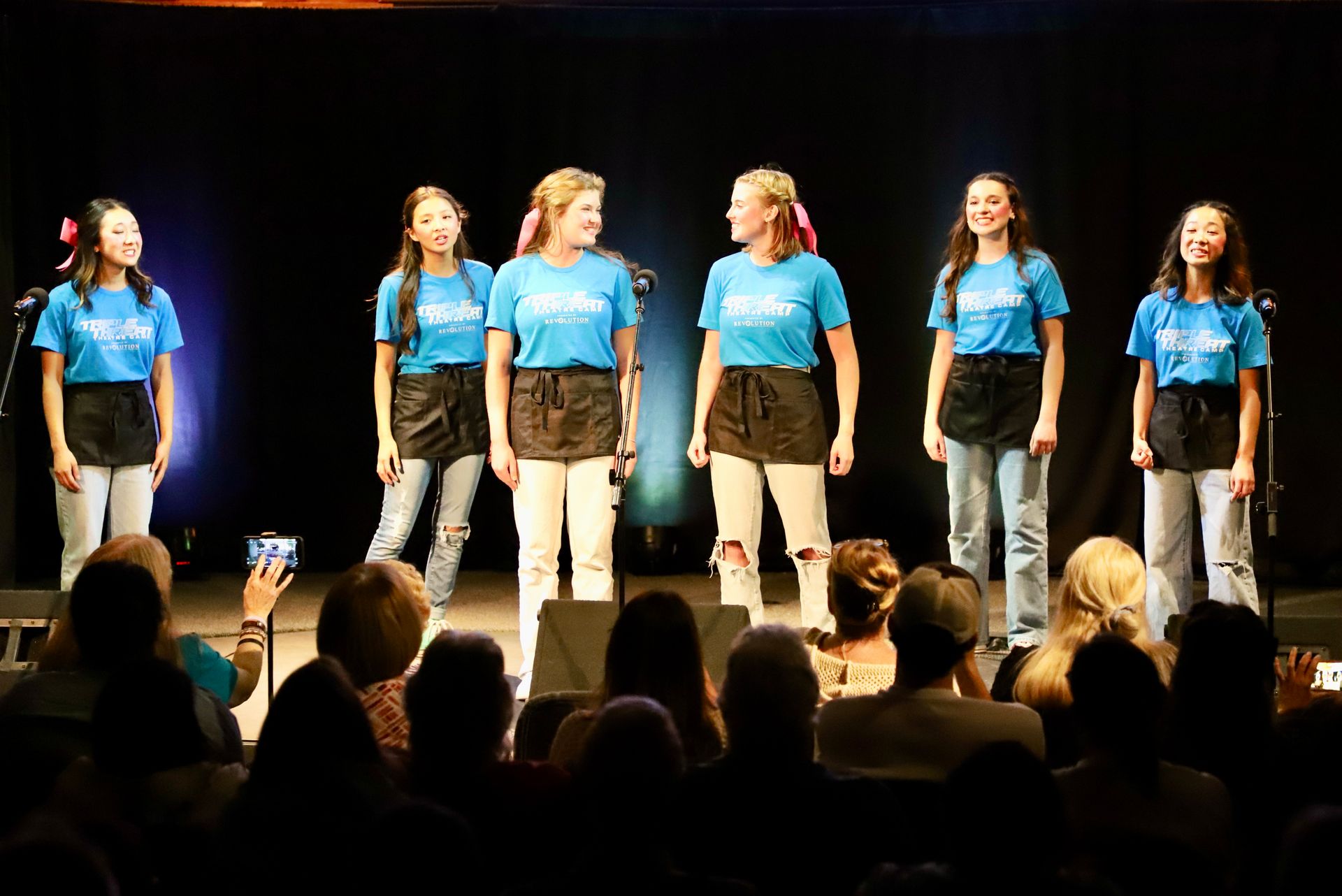 A group of young women are singing on a stage in front of a crowd.