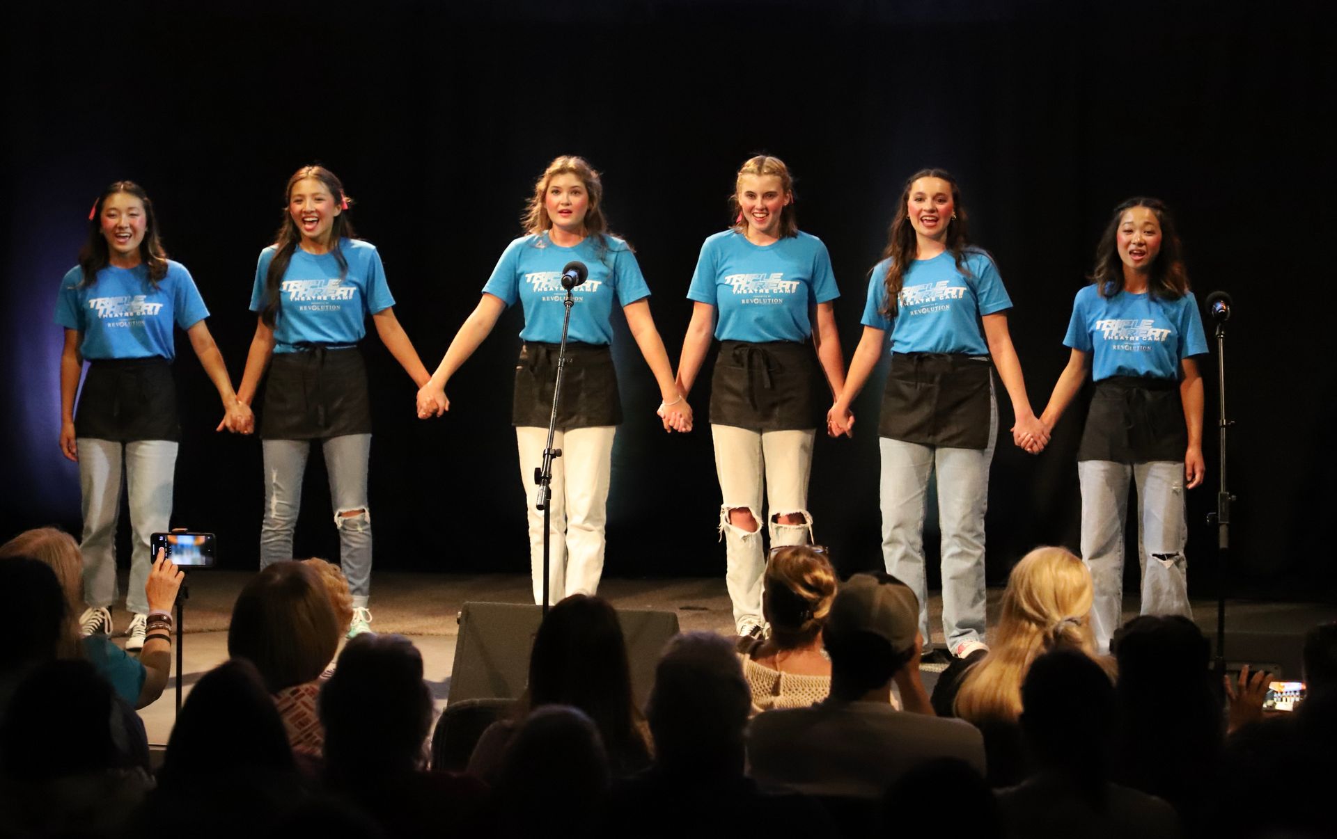 A group of girls are holding hands on a stage in front of a crowd.