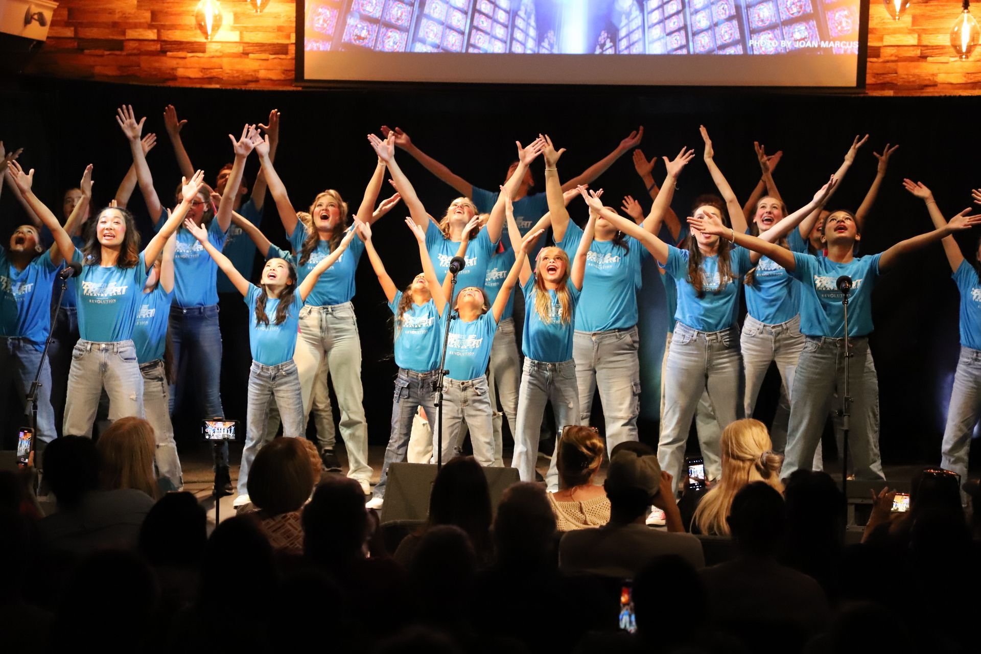A group of young girls are standing on a stage with their arms in the air.