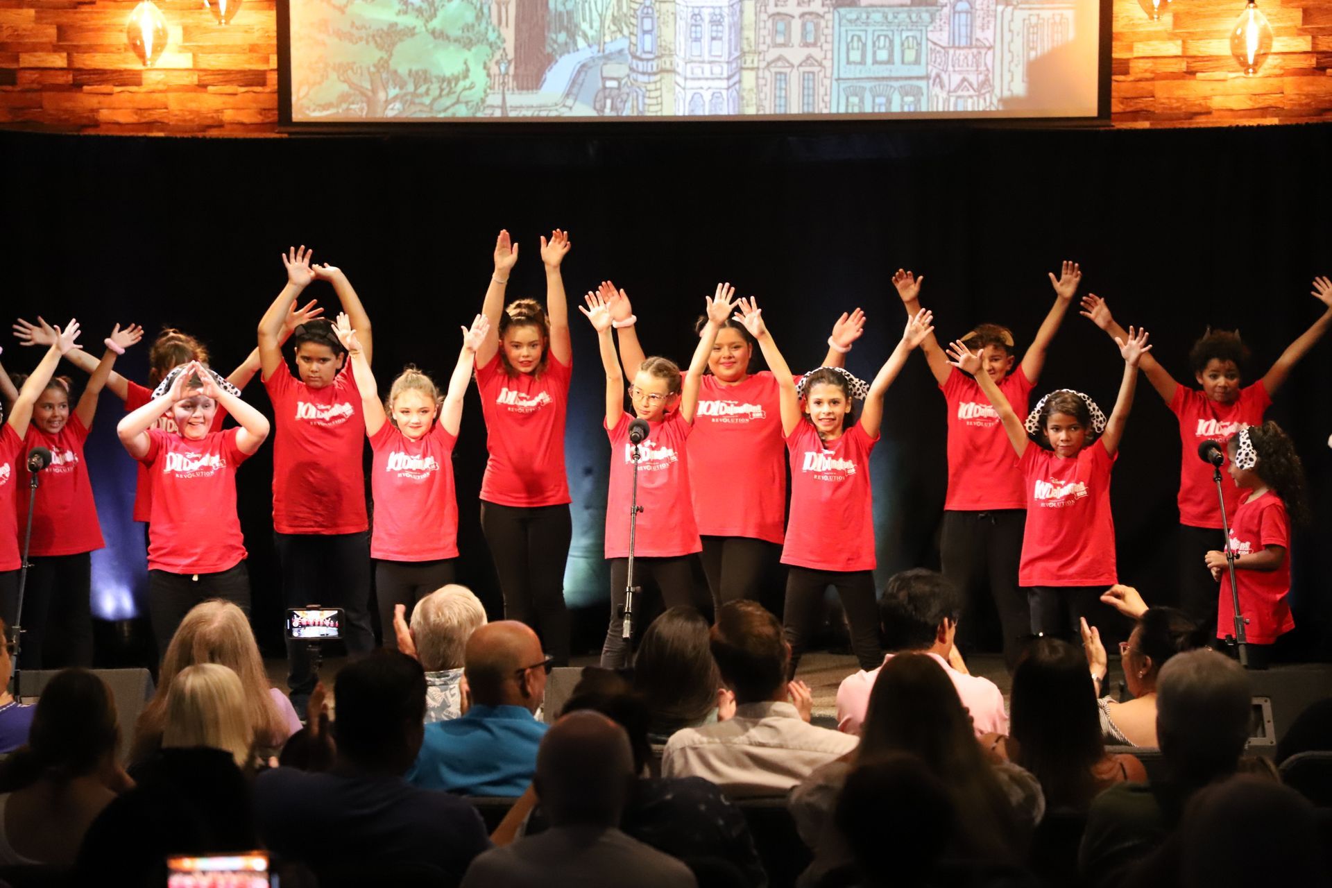 A group of children are standing on a stage with their hands in the air.