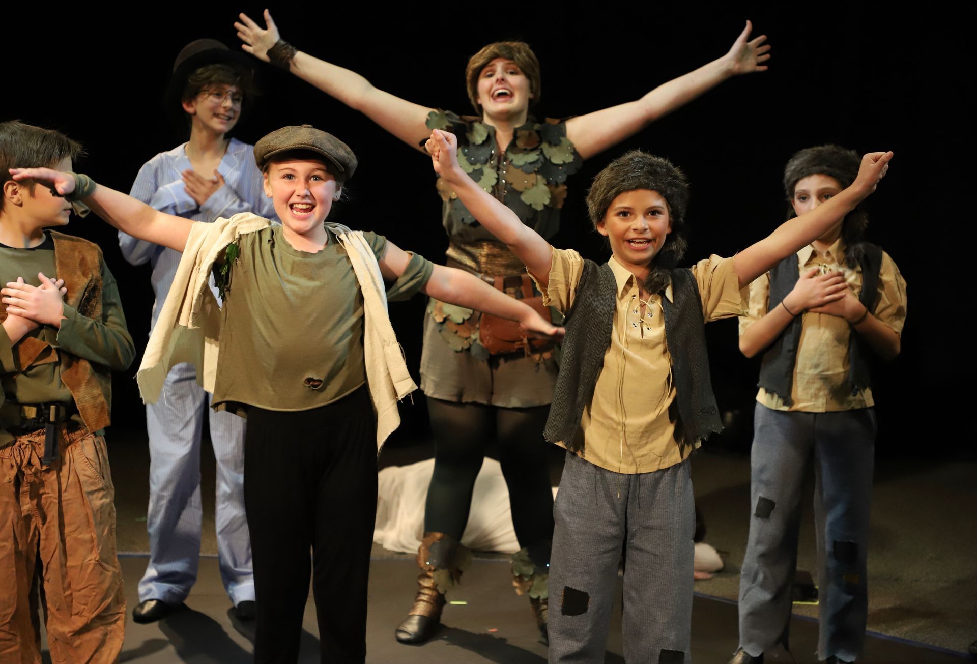 A group of children are standing on a stage with their arms outstretched