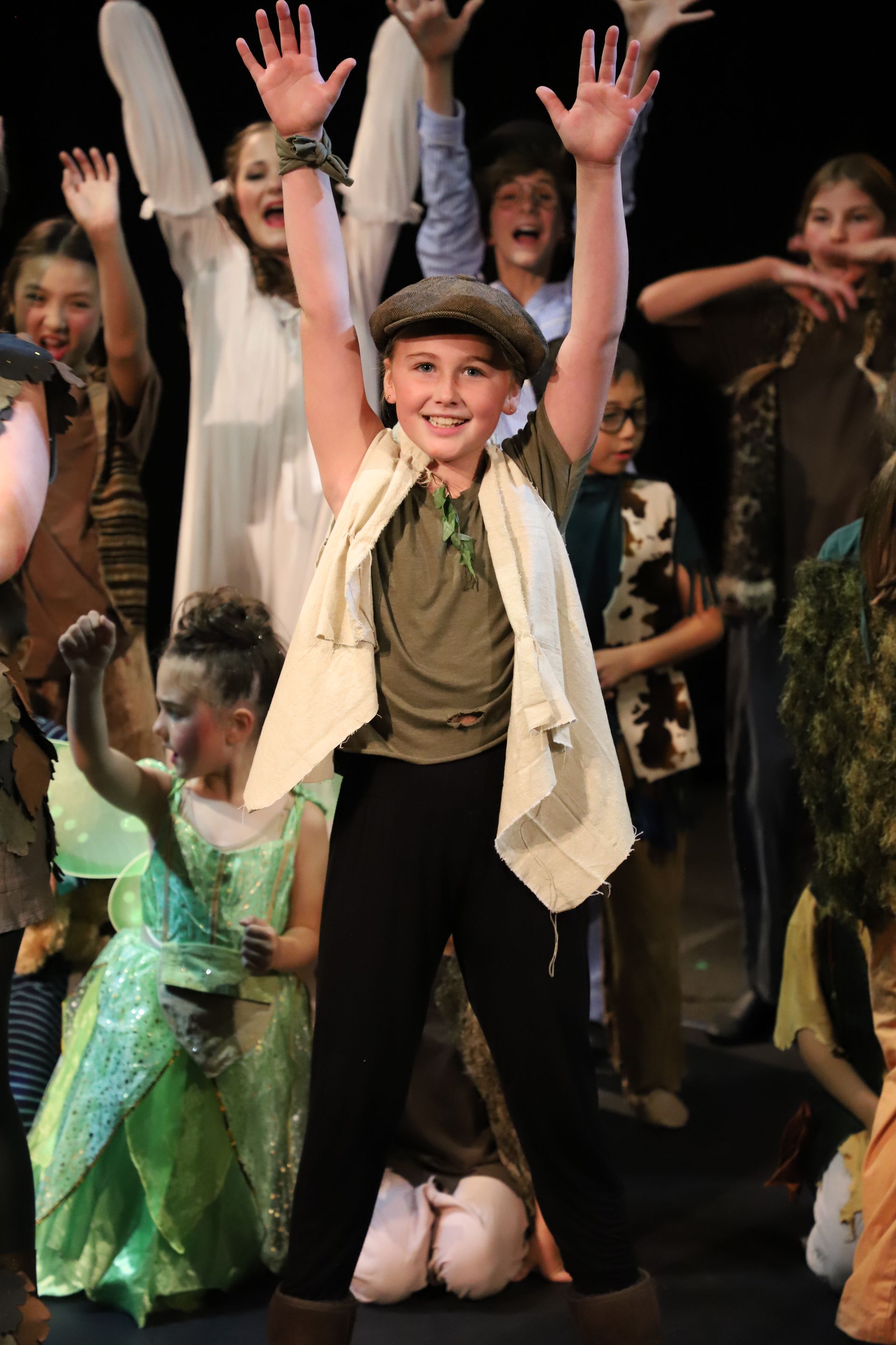 A group of children are standing on a stage with their hands in the air.