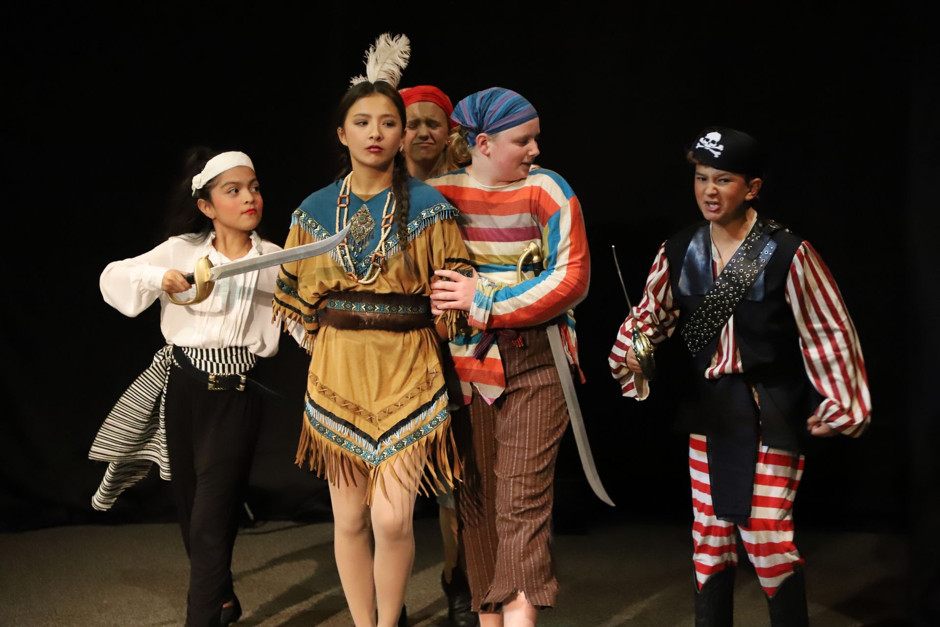 A group of children dressed in pirate costumes are standing on a stage.