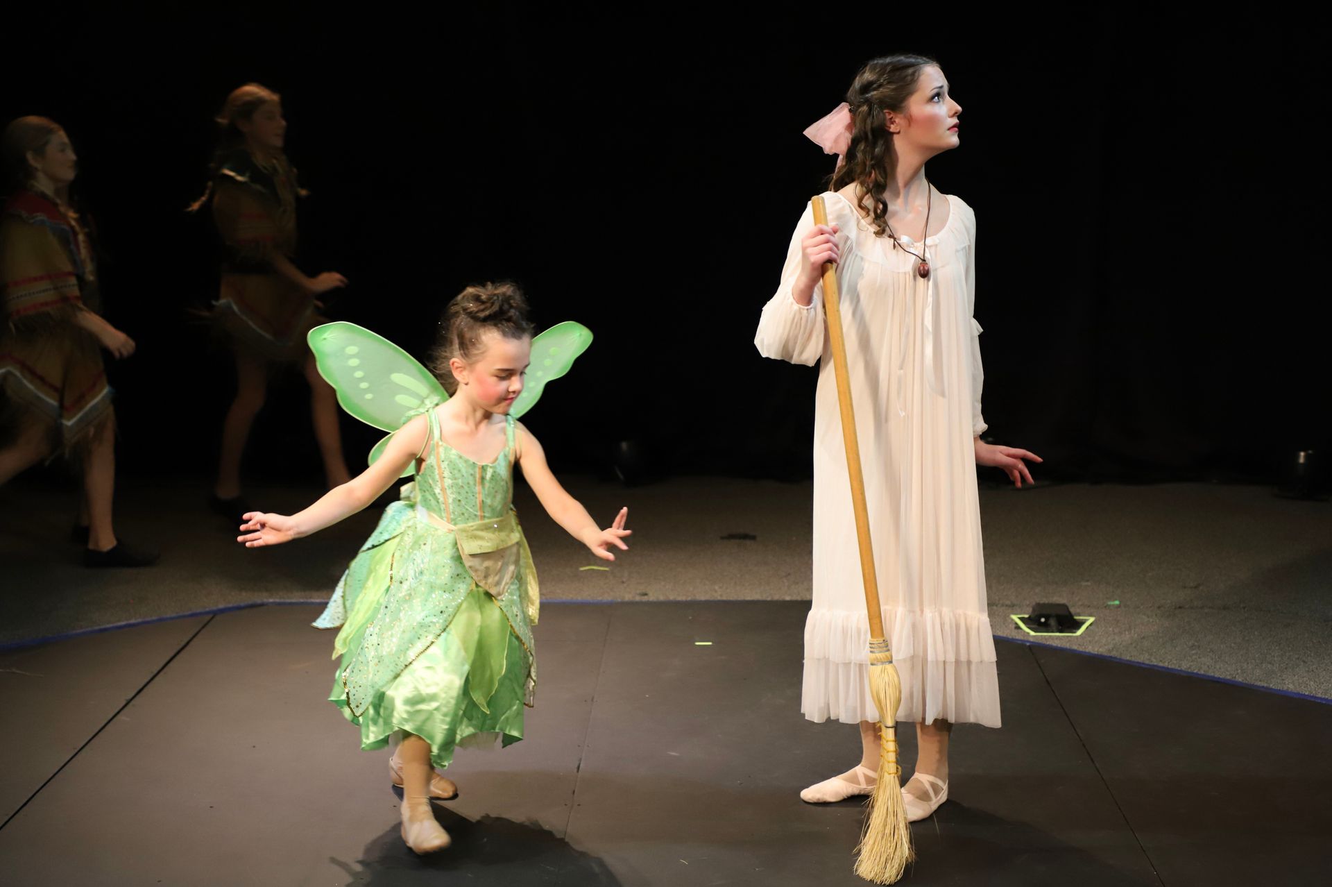 A little girl in a fairy costume is standing next to a woman in a white dress on a stage.