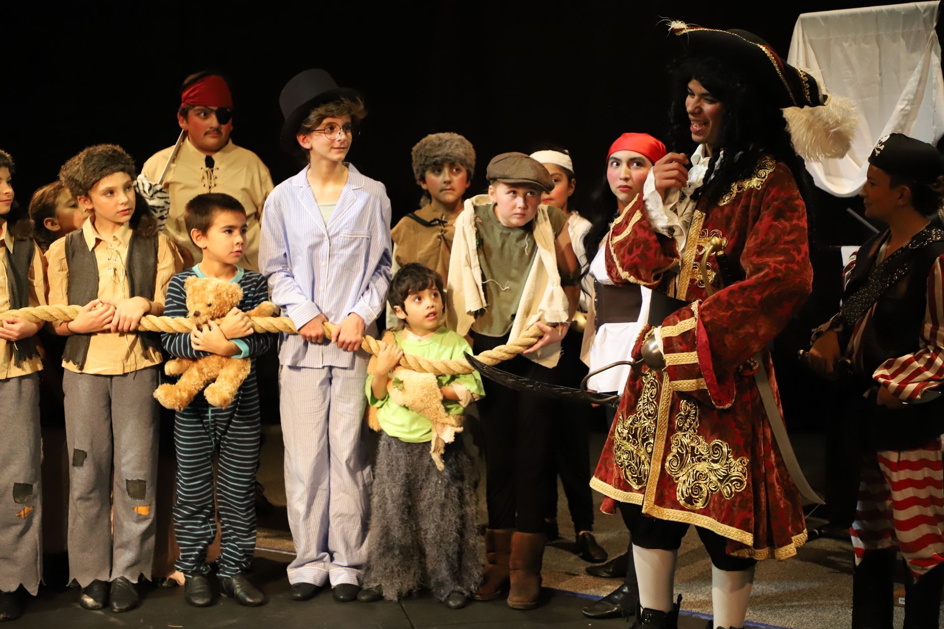 A man in a pirate costume is standing in front of a group of children holding teddy bears.