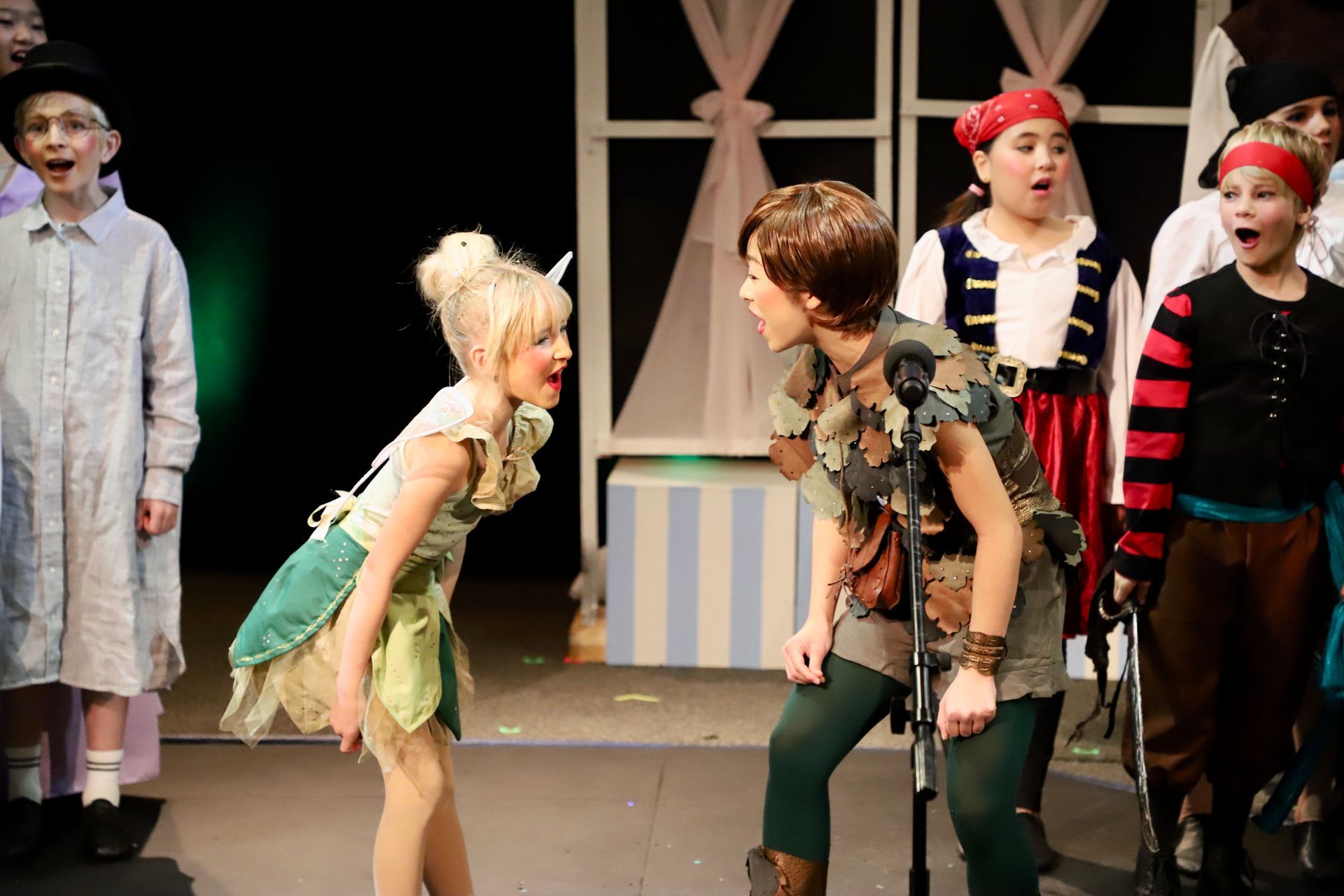A group of children are playing peter pan and tinkerbell on a stage.