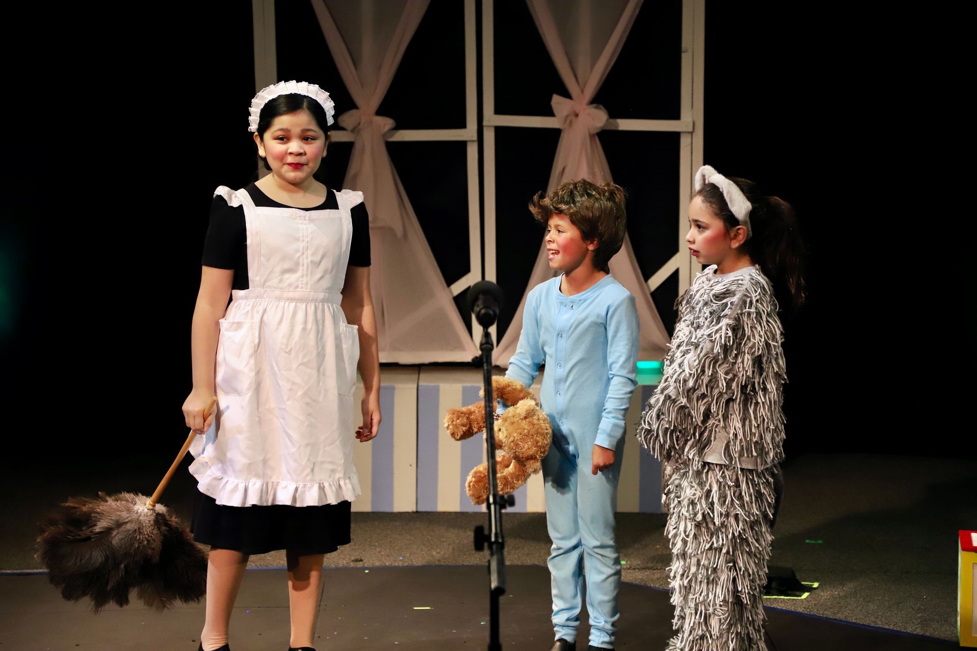 A girl in an apron is holding a broom next to two children.