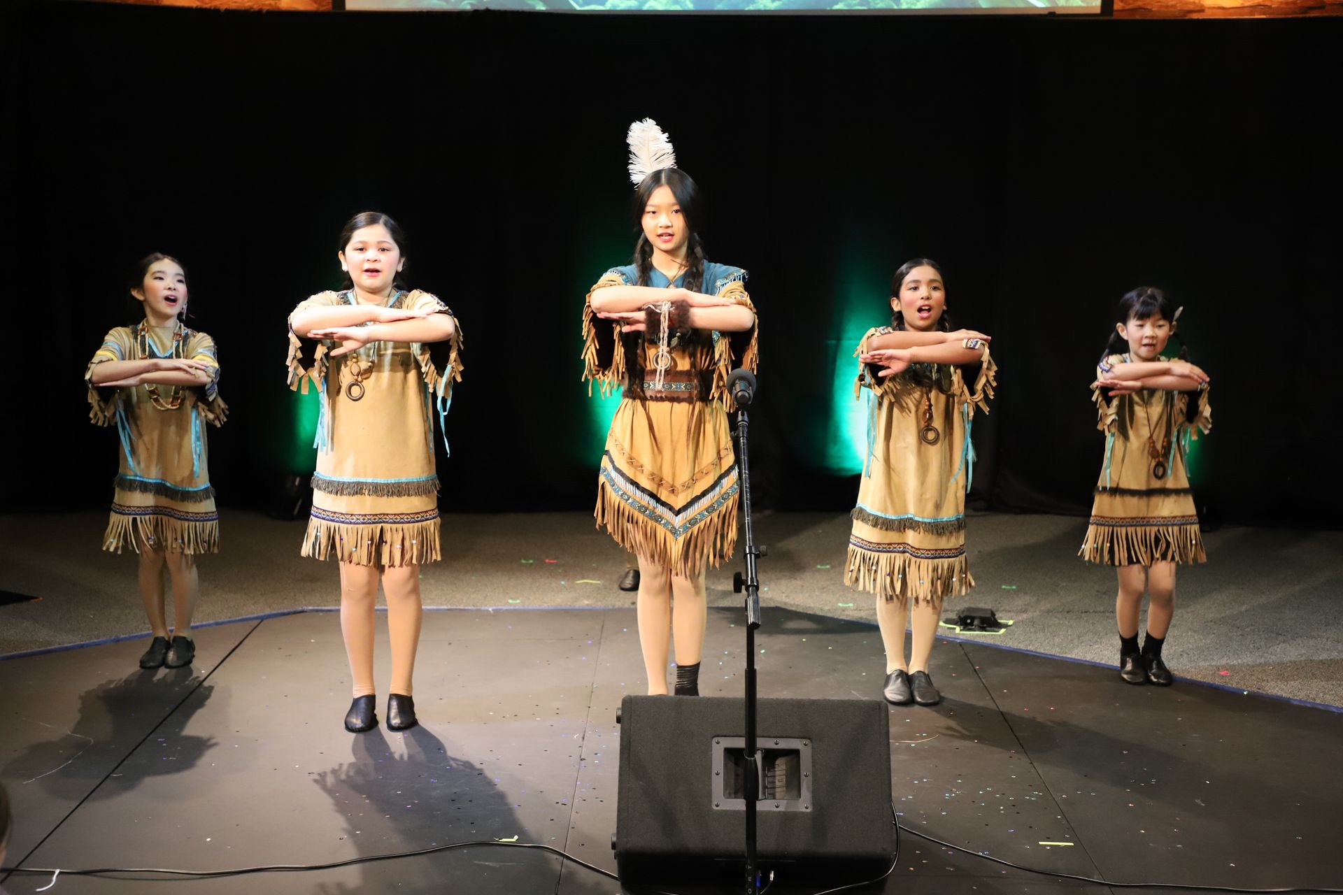 A group of young girls in native american costumes are dancing on a stage.