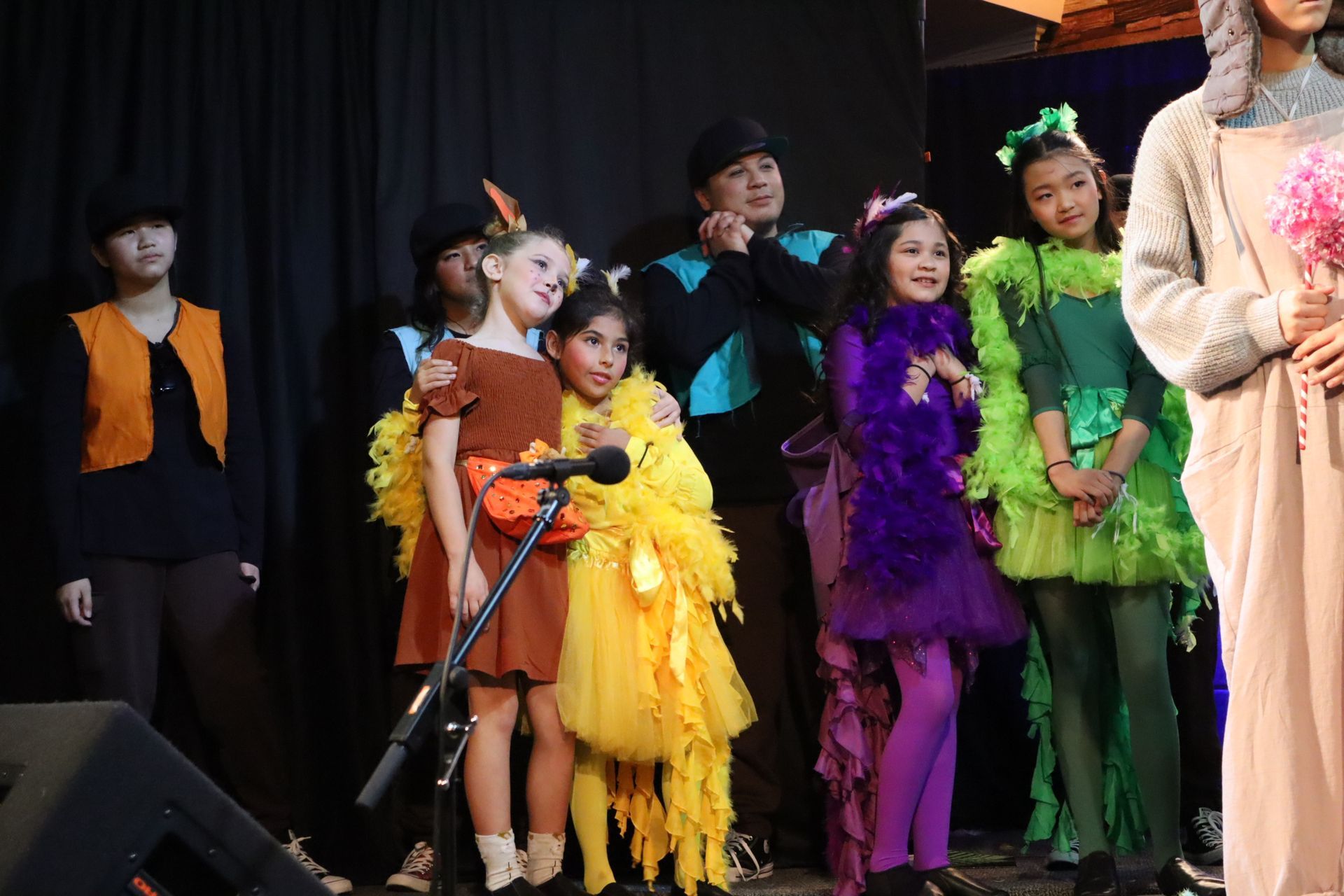 A group of children in costumes are standing in front of a microphone on a stage.