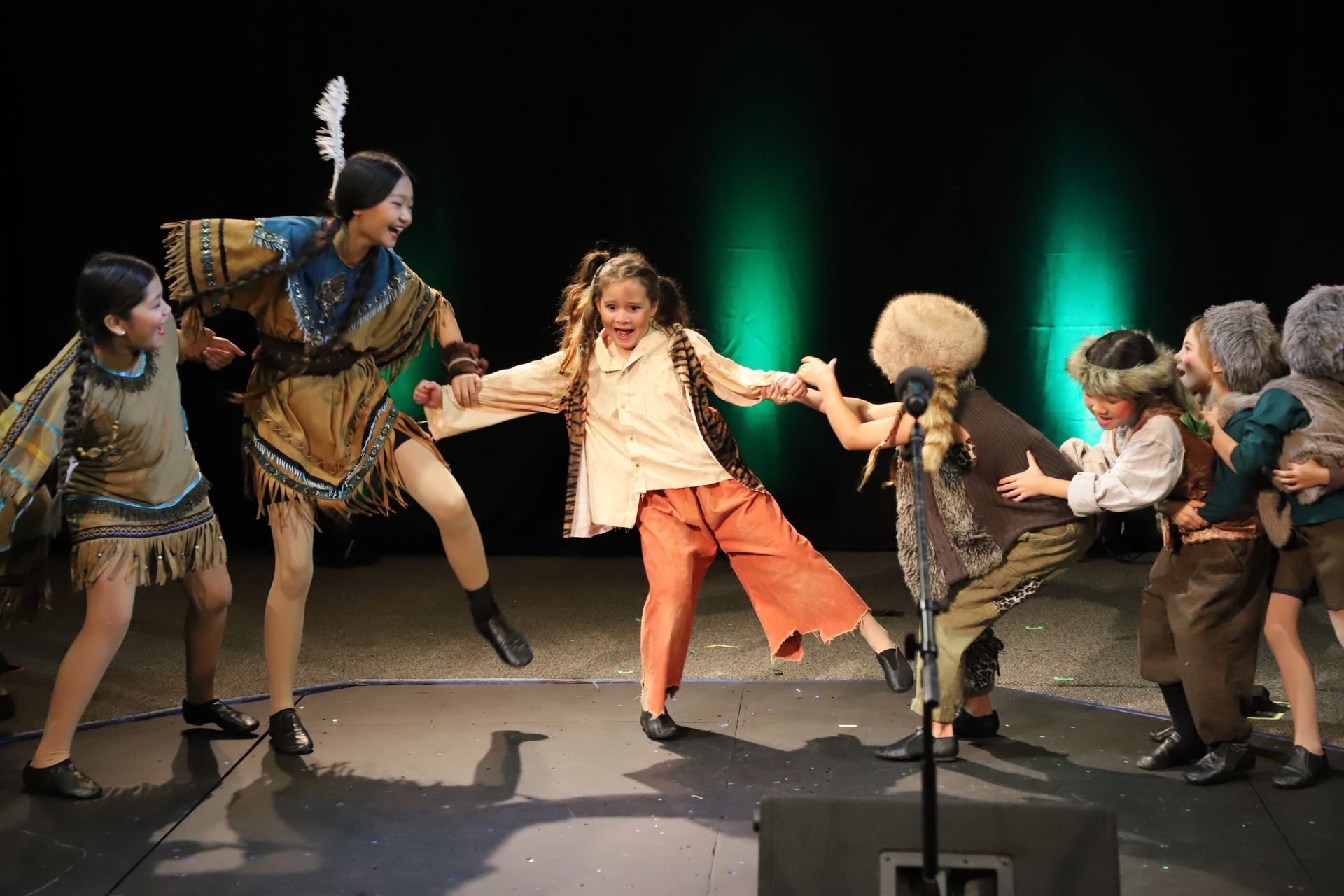 A group of children in native american costumes are dancing on a stage.