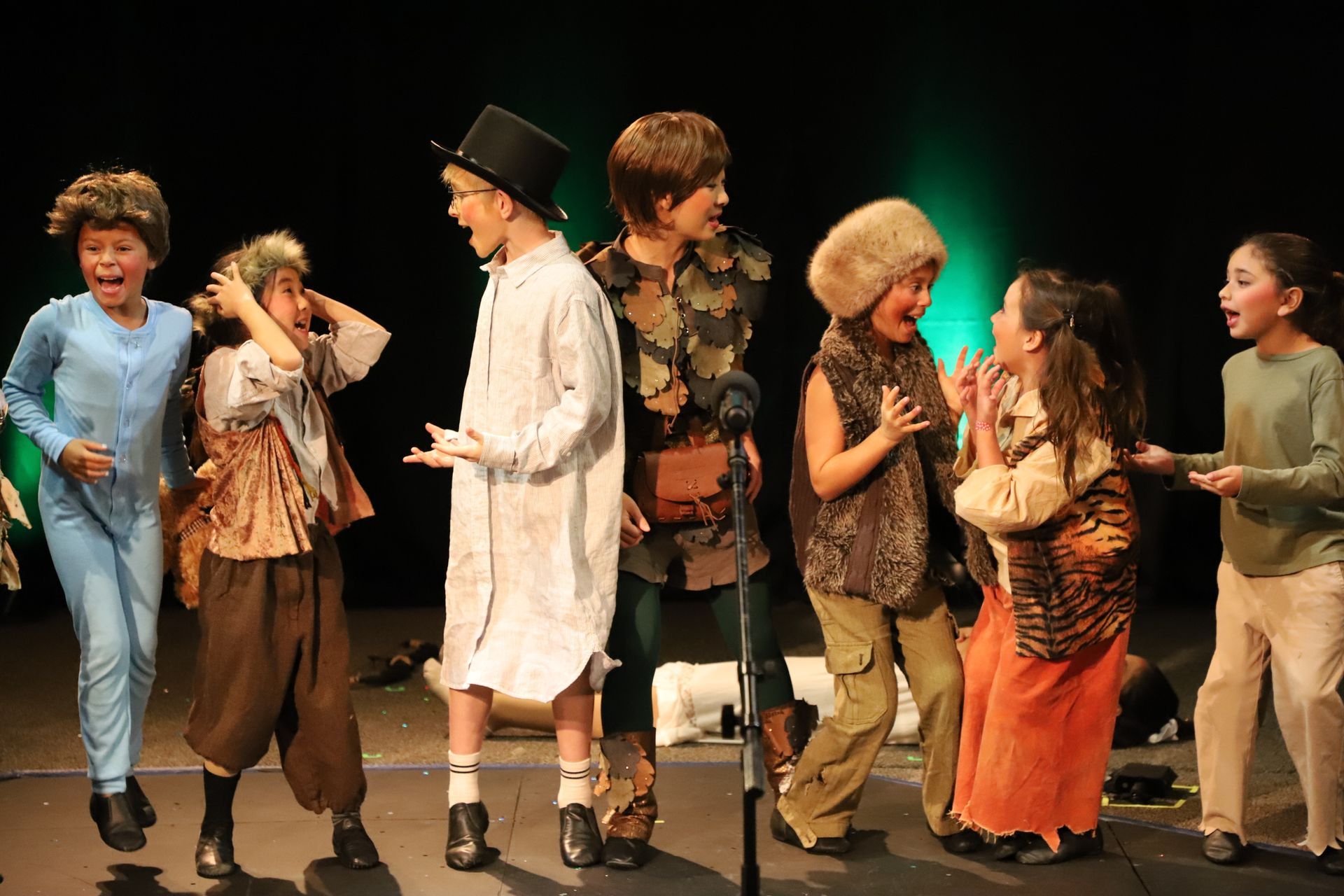 A group of children are standing on a stage in front of a microphone.