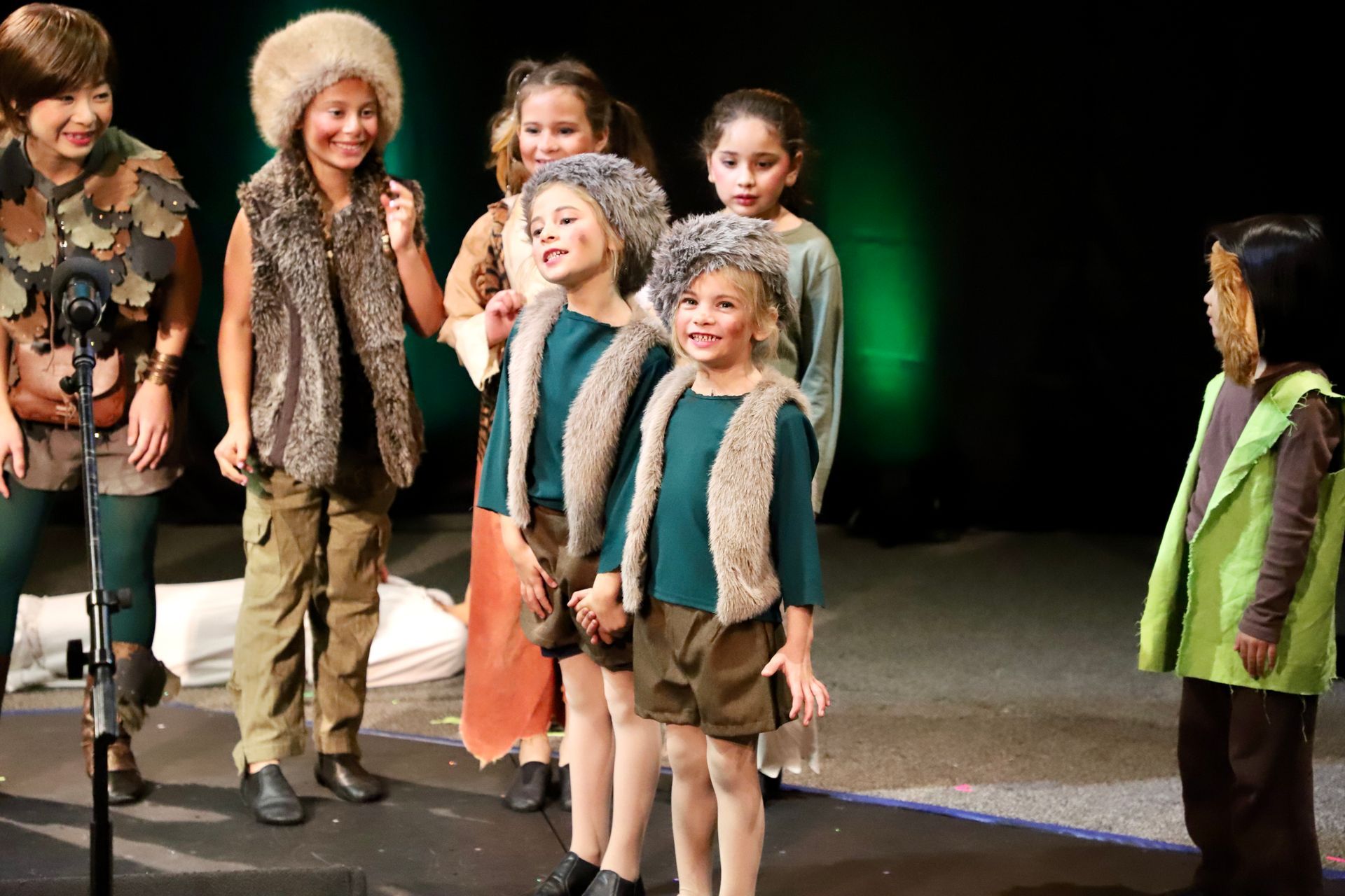 A group of children are standing on a stage in front of a microphone.