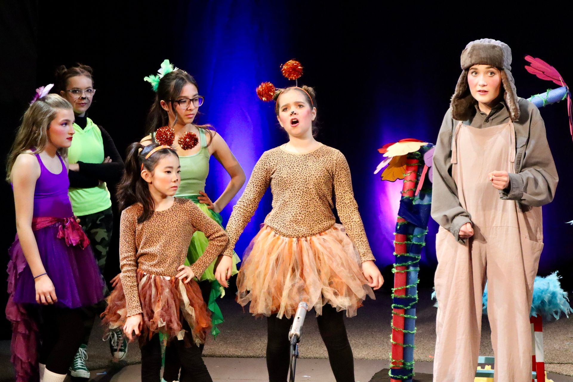 A group of young girls are standing on a stage in costumes.