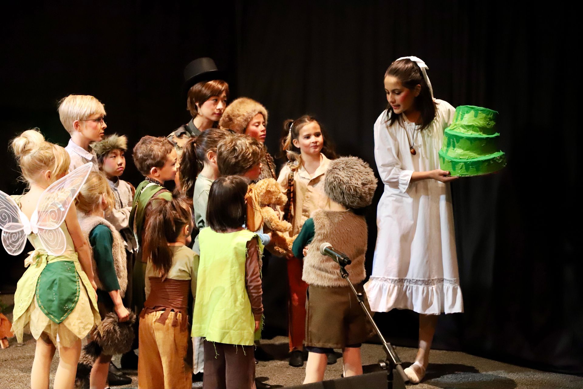 A woman is holding a green cake in front of a group of children.