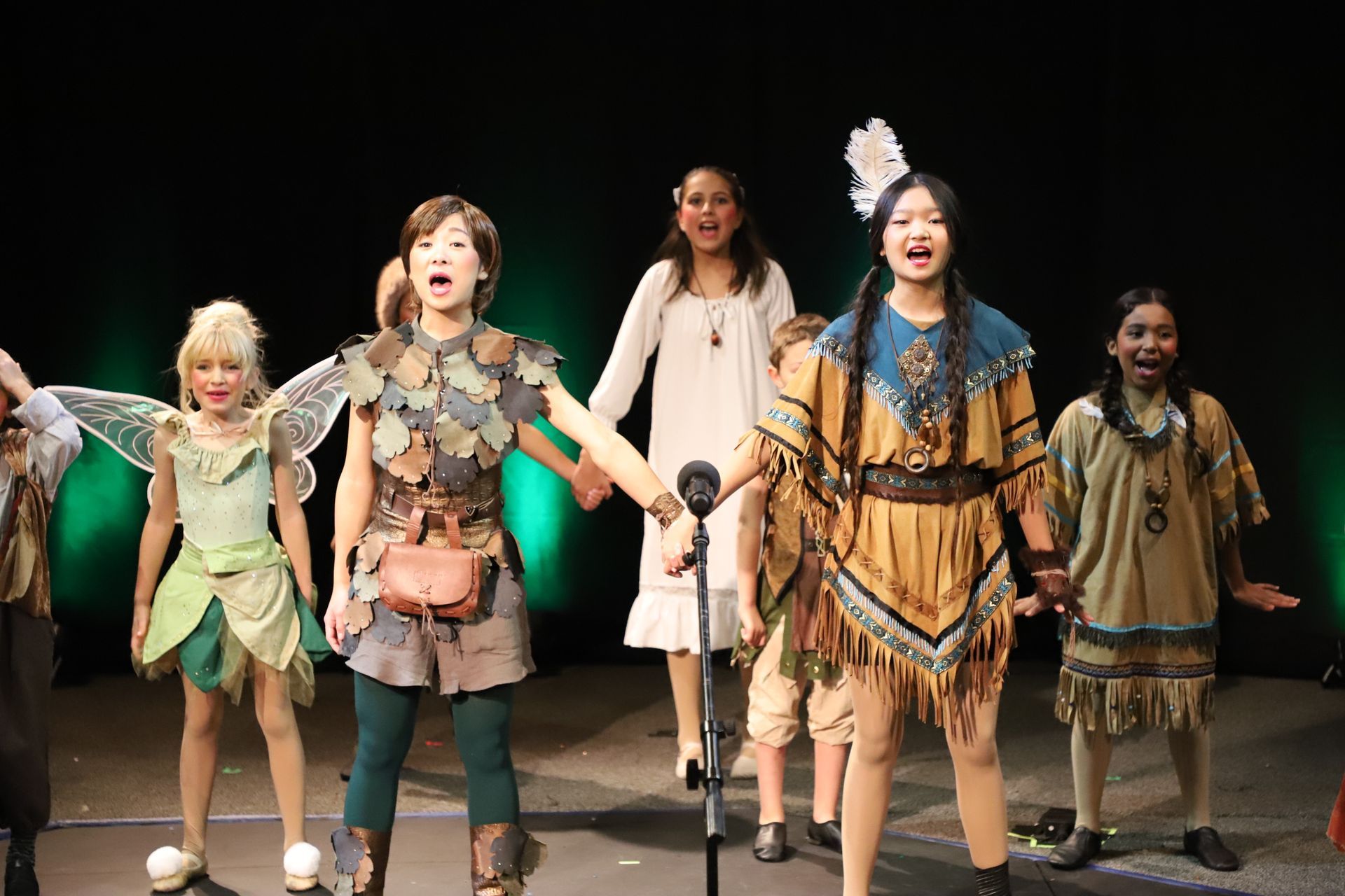 A group of children in costume are singing into a microphone on a stage.
