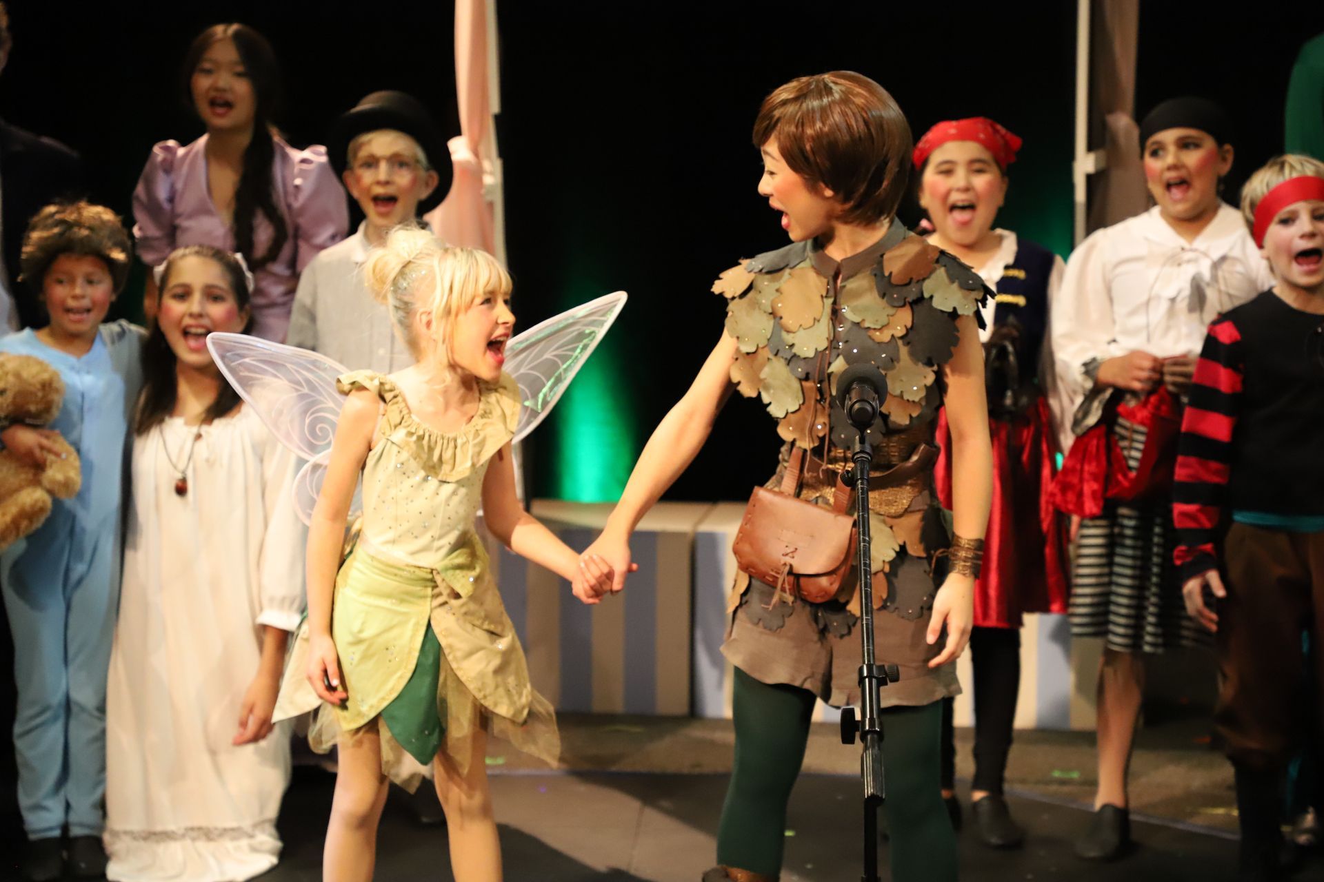 A group of children dressed in costumes are standing on a stage holding hands.