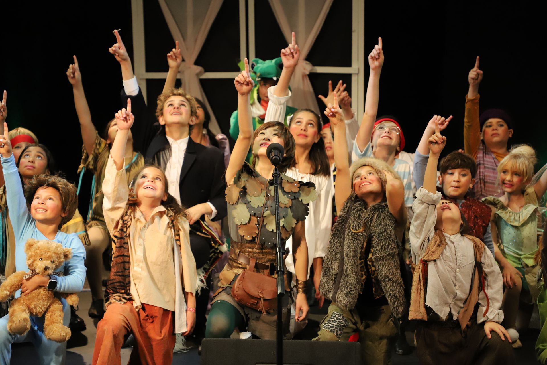 A group of children are standing on a stage with their hands in the air.