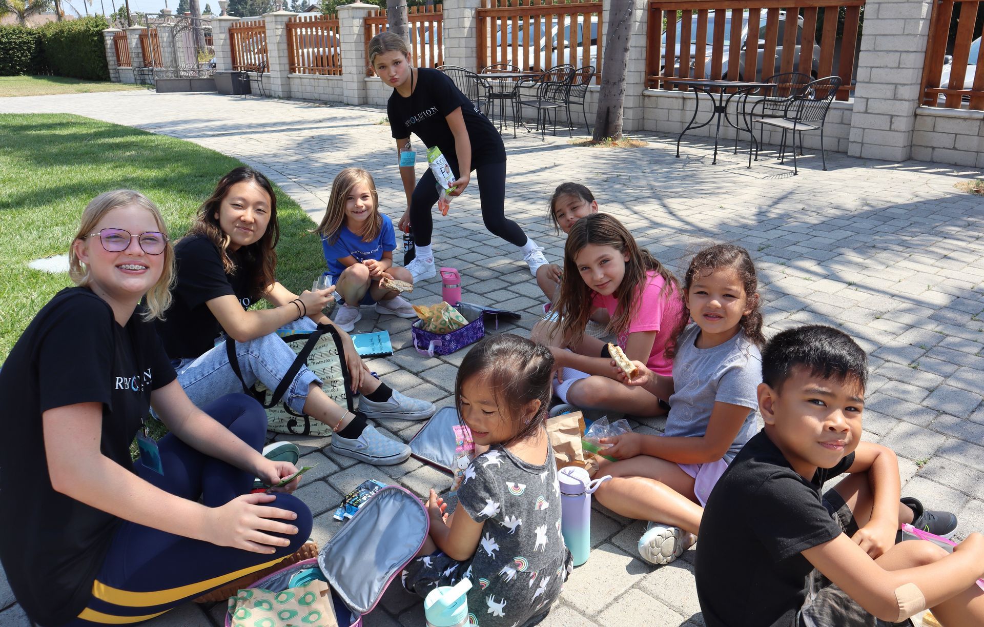 A group of children are sitting on the ground eating ice cream.