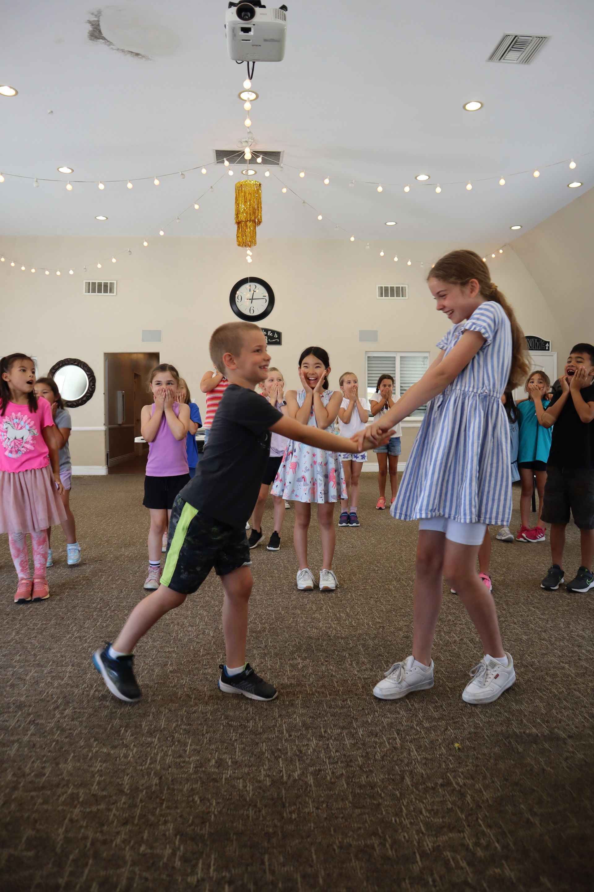 A boy and a girl are dancing in a room with other children.