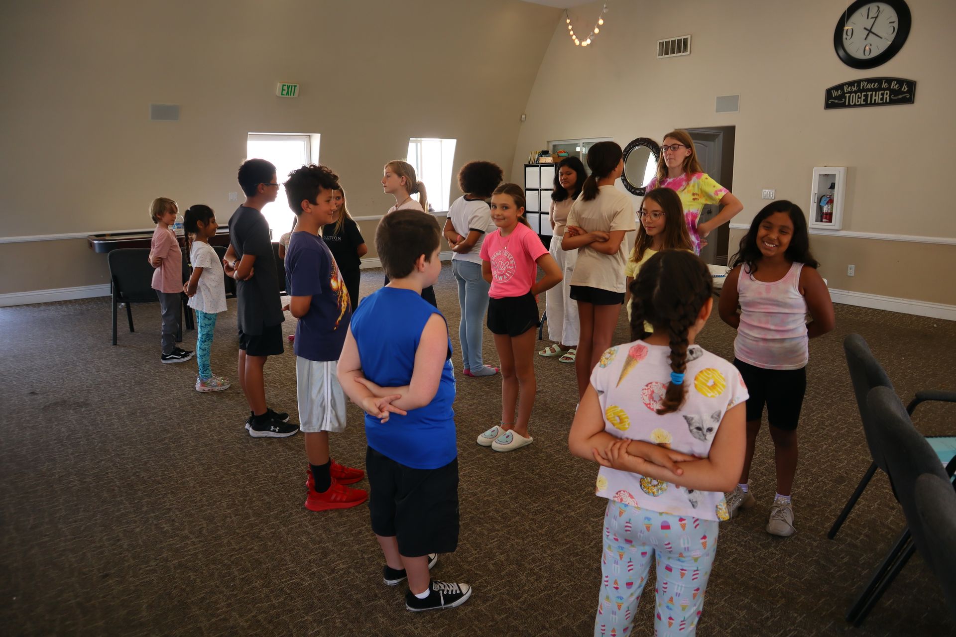 A group of children are standing in a room with a clock on the wall.