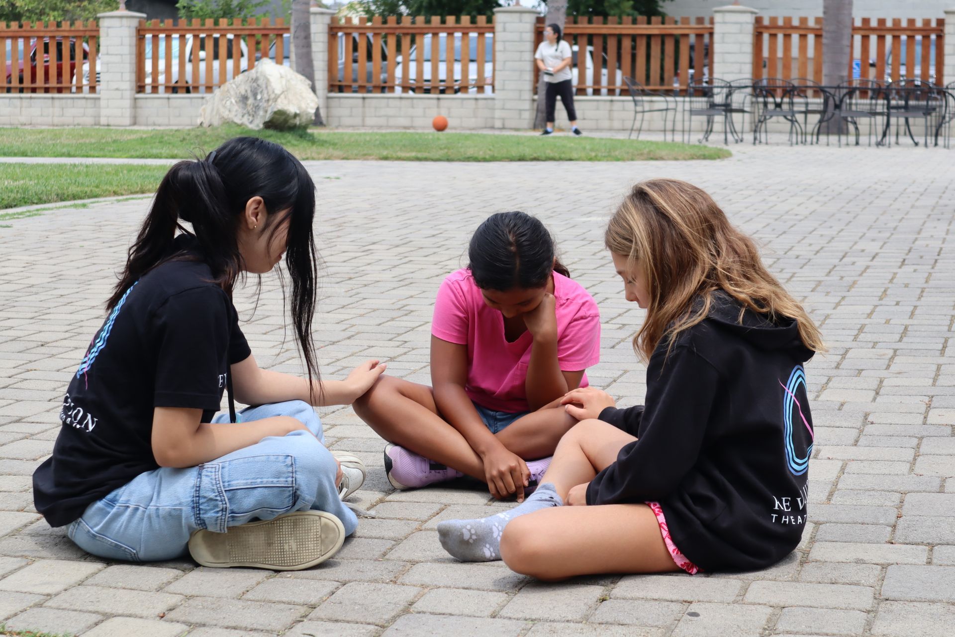 Three young girls are sitting on the ground in a circle.