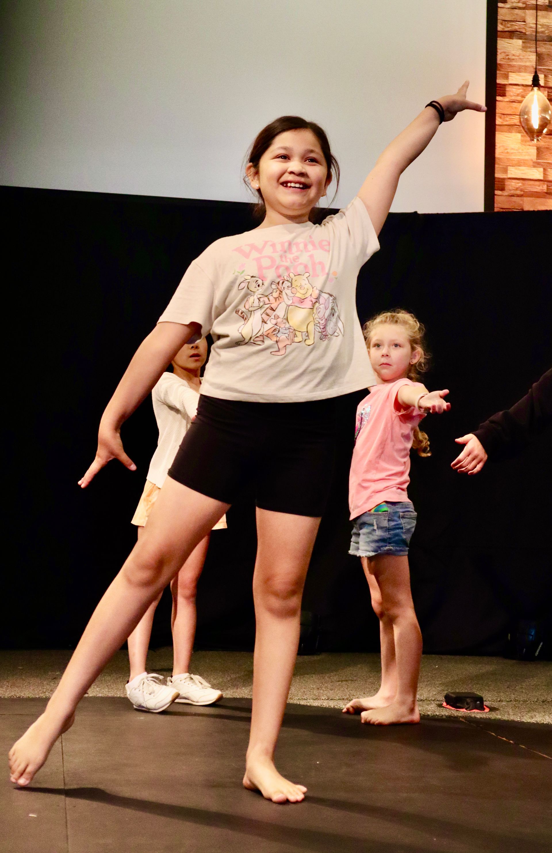 A young girl is standing on a balance beam with her arm in the air.