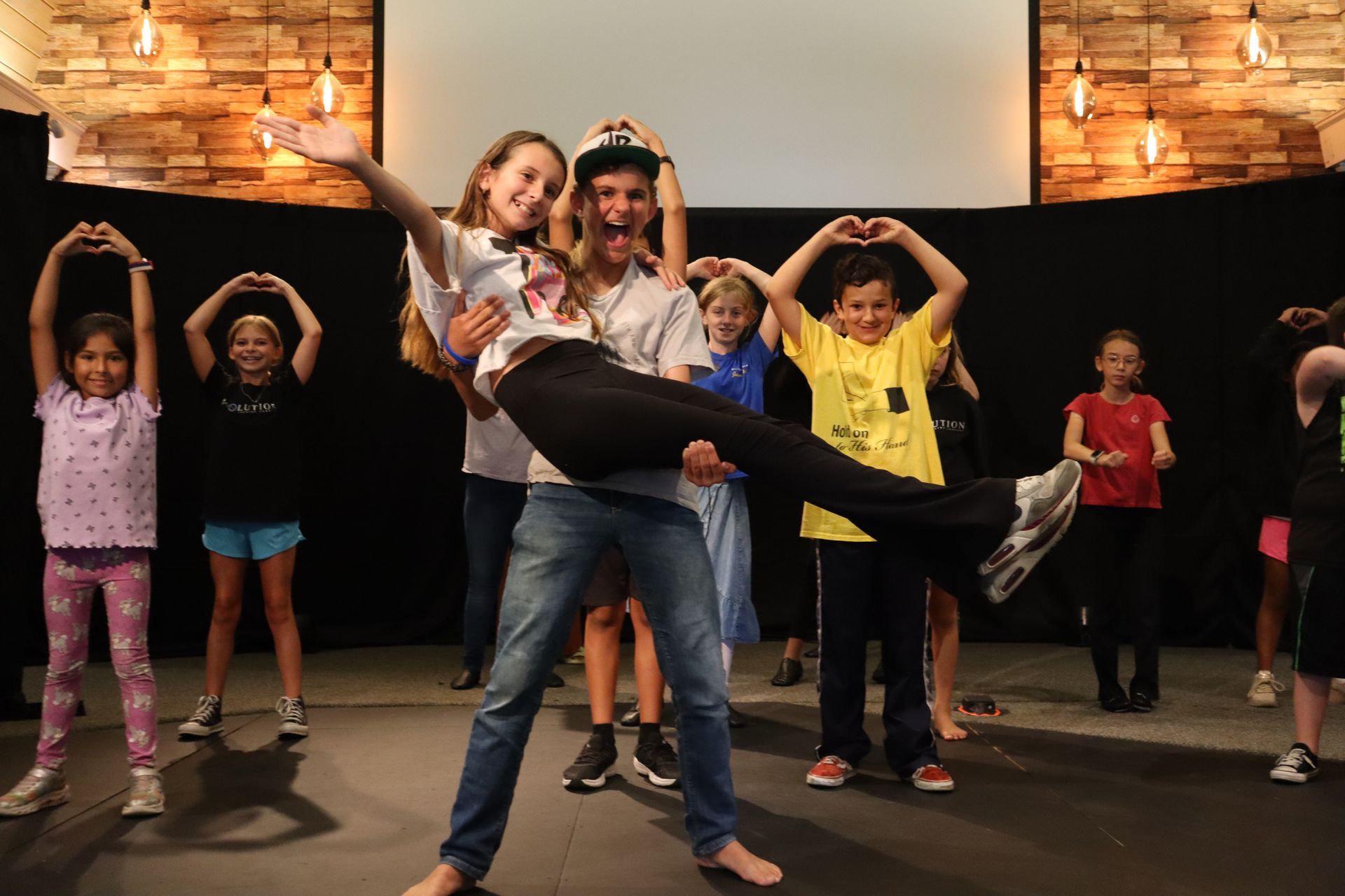 A man is holding a woman in his arms while a group of children are dancing.
