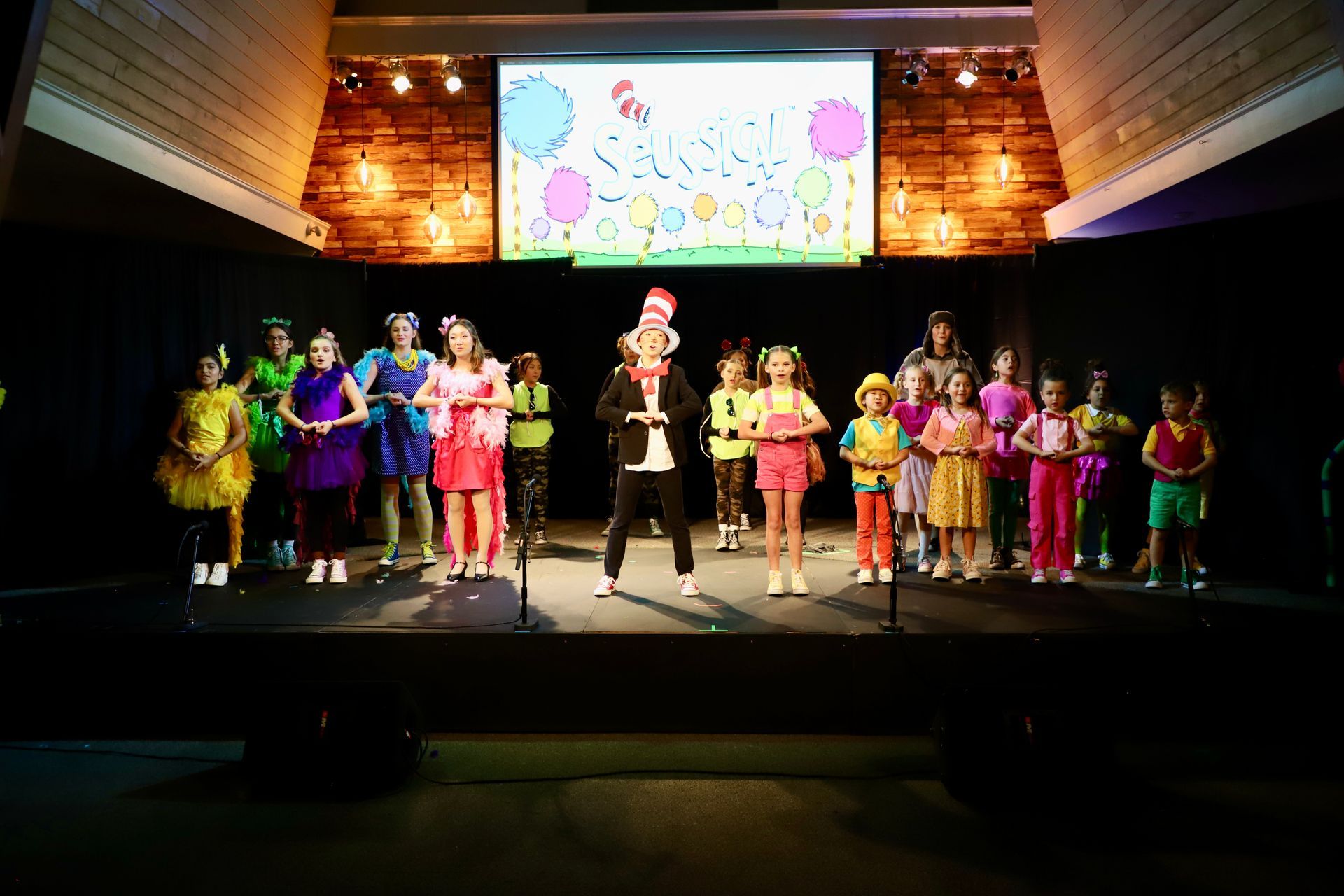 A group of children are standing on a stage in front of a large screen.
