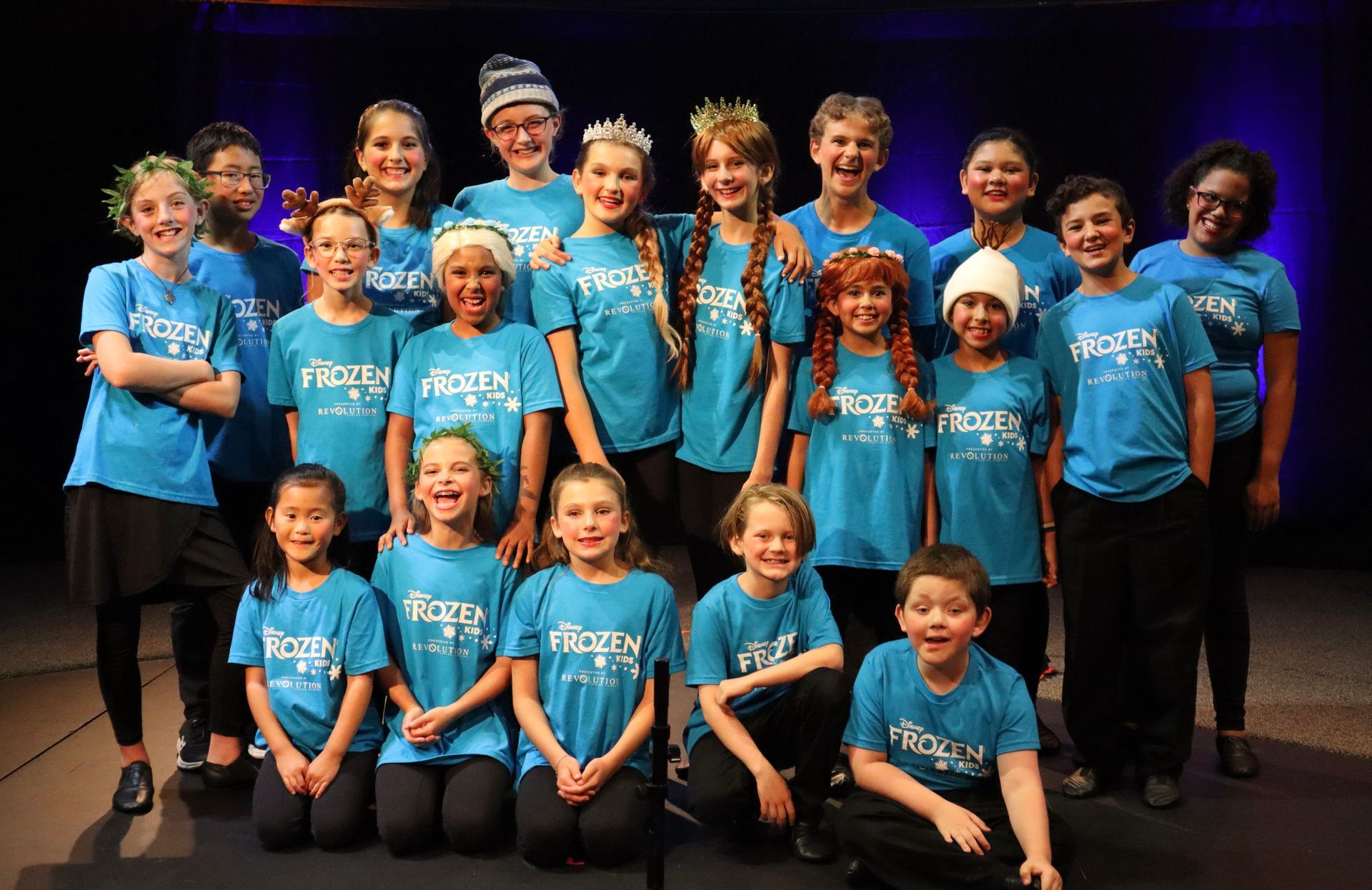 A group of children wearing blue shirts are posing for a picture.