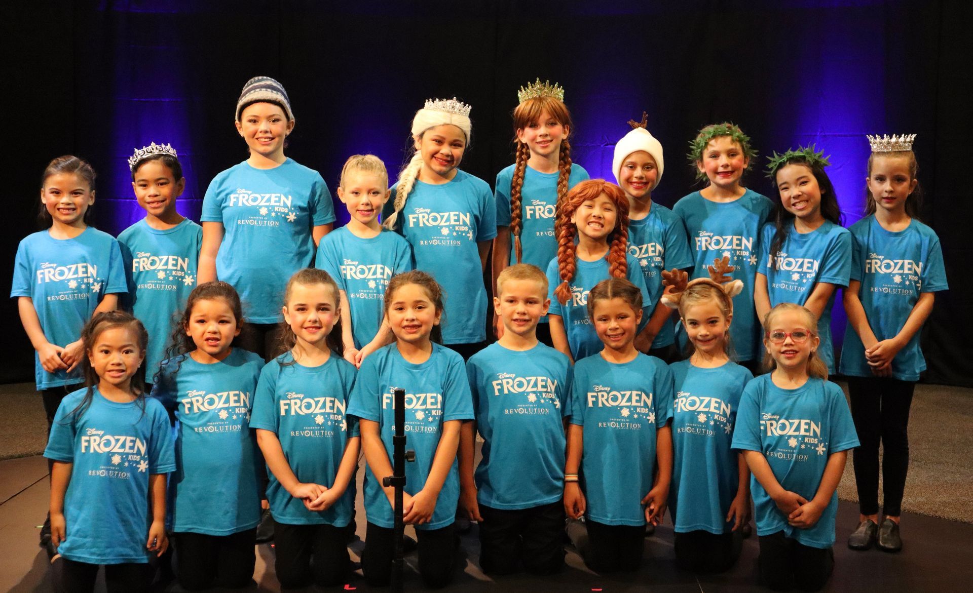 A group of children wearing blue shirts are posing for a picture on a stage.