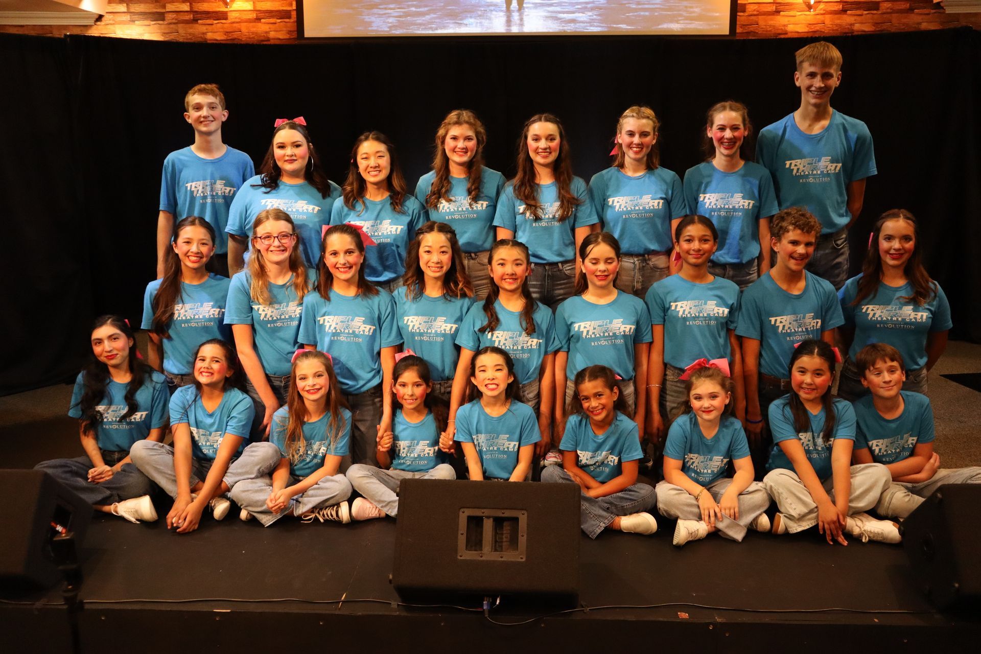 A group of children in blue shirts are posing for a picture on a stage.