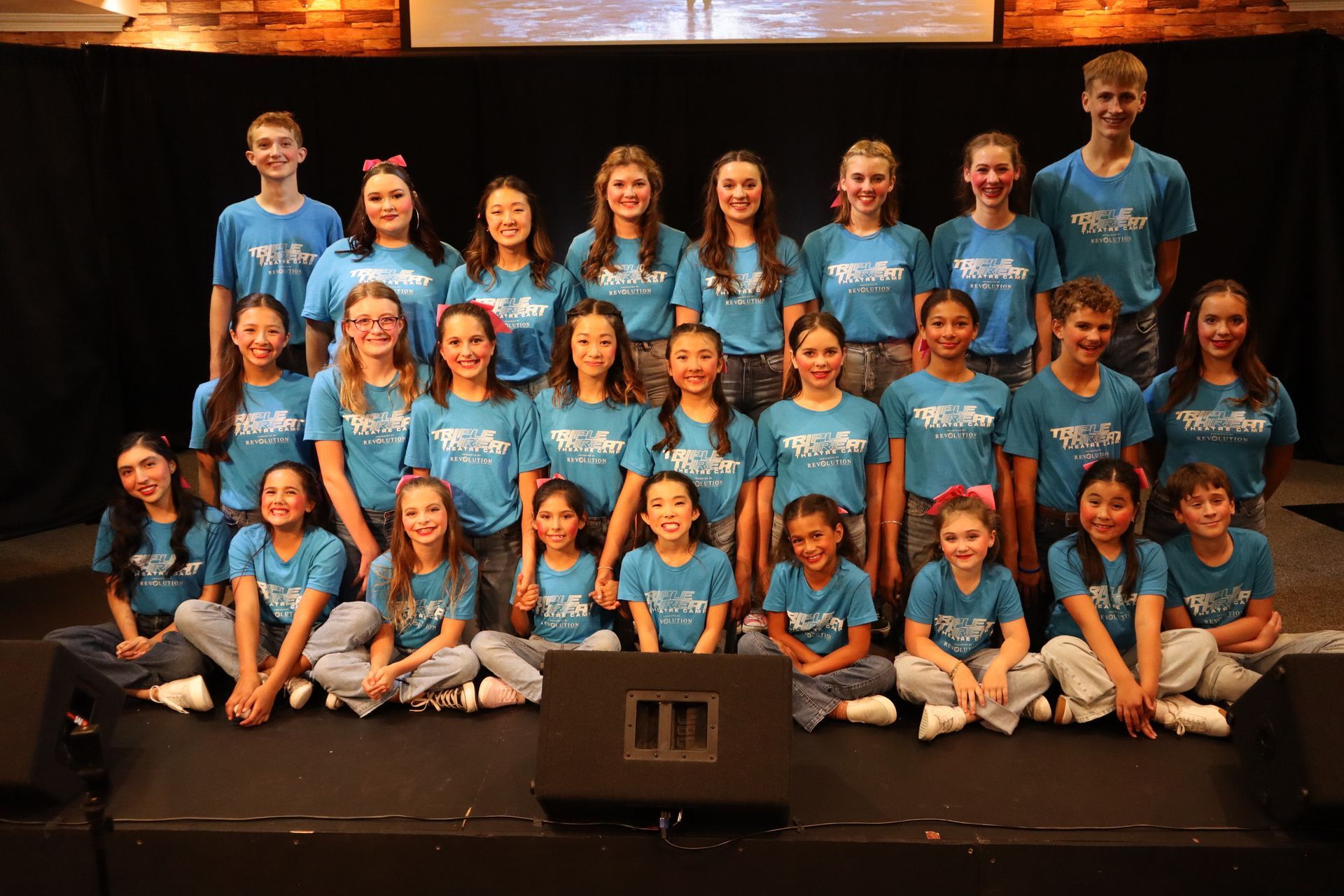 A group of children in blue shirts are posing for a picture on a stage.