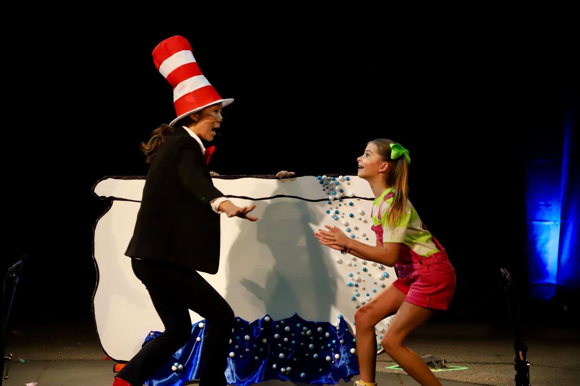 A man in a cat in the hat is standing next to a girl on a stage.