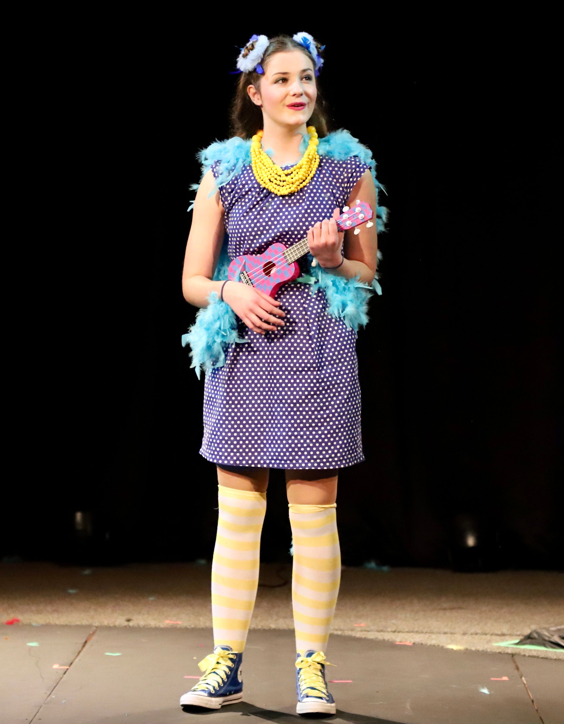 A woman in a purple dress is holding an ukulele on a stage.