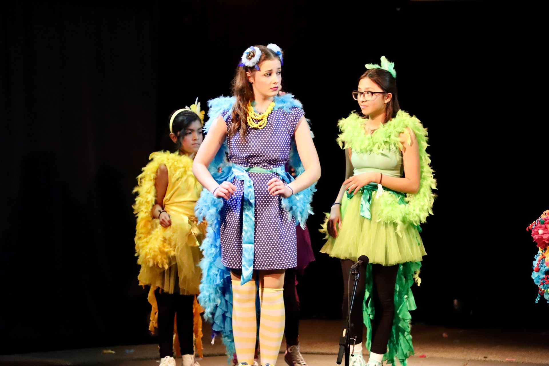 A group of young girls dressed in colorful costumes are standing on a stage.