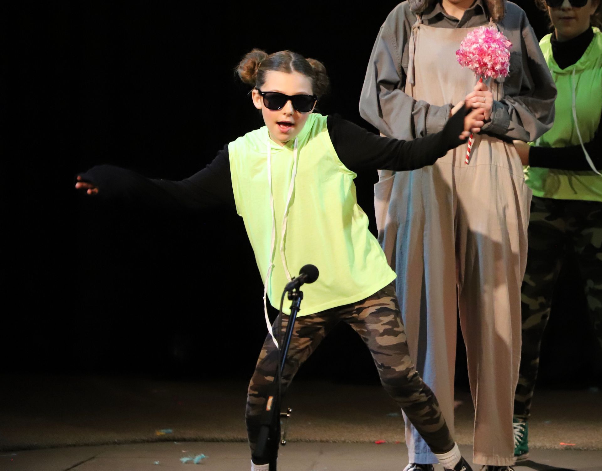 A little girl is singing into a microphone while wearing sunglasses.