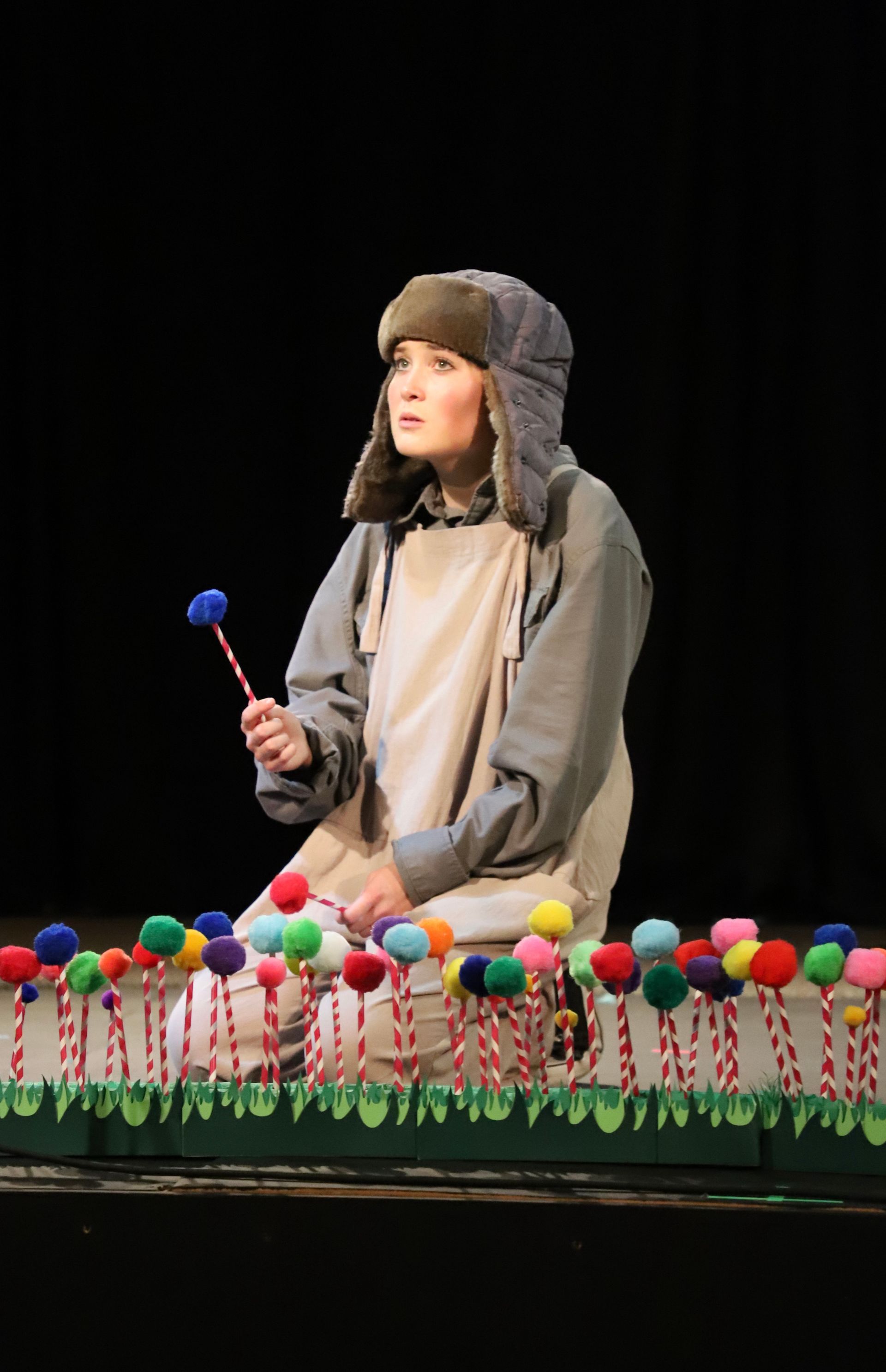 A woman is sitting on a stage holding a lollipop.