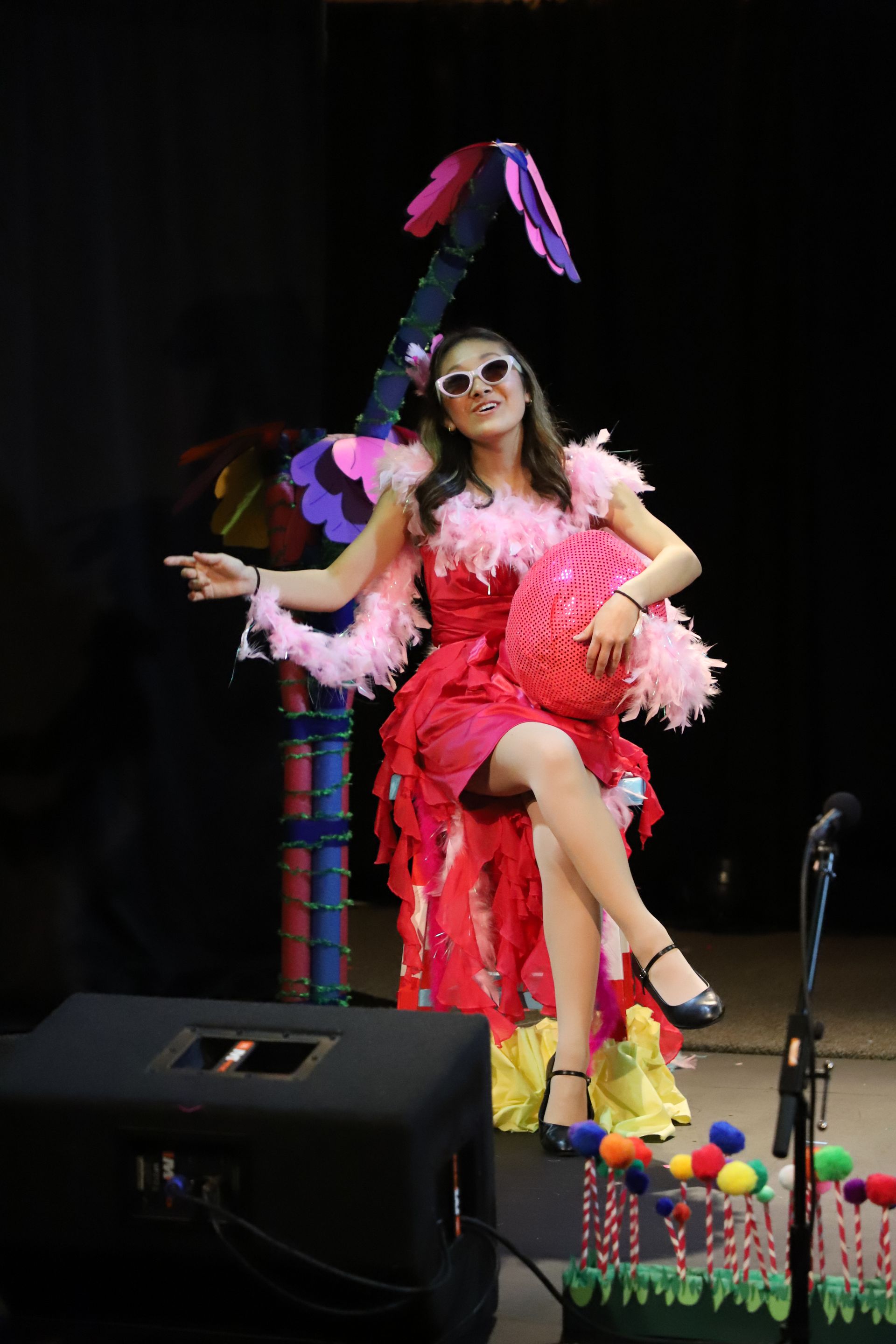 A woman in a red dress is sitting on a chair in front of a microphone.