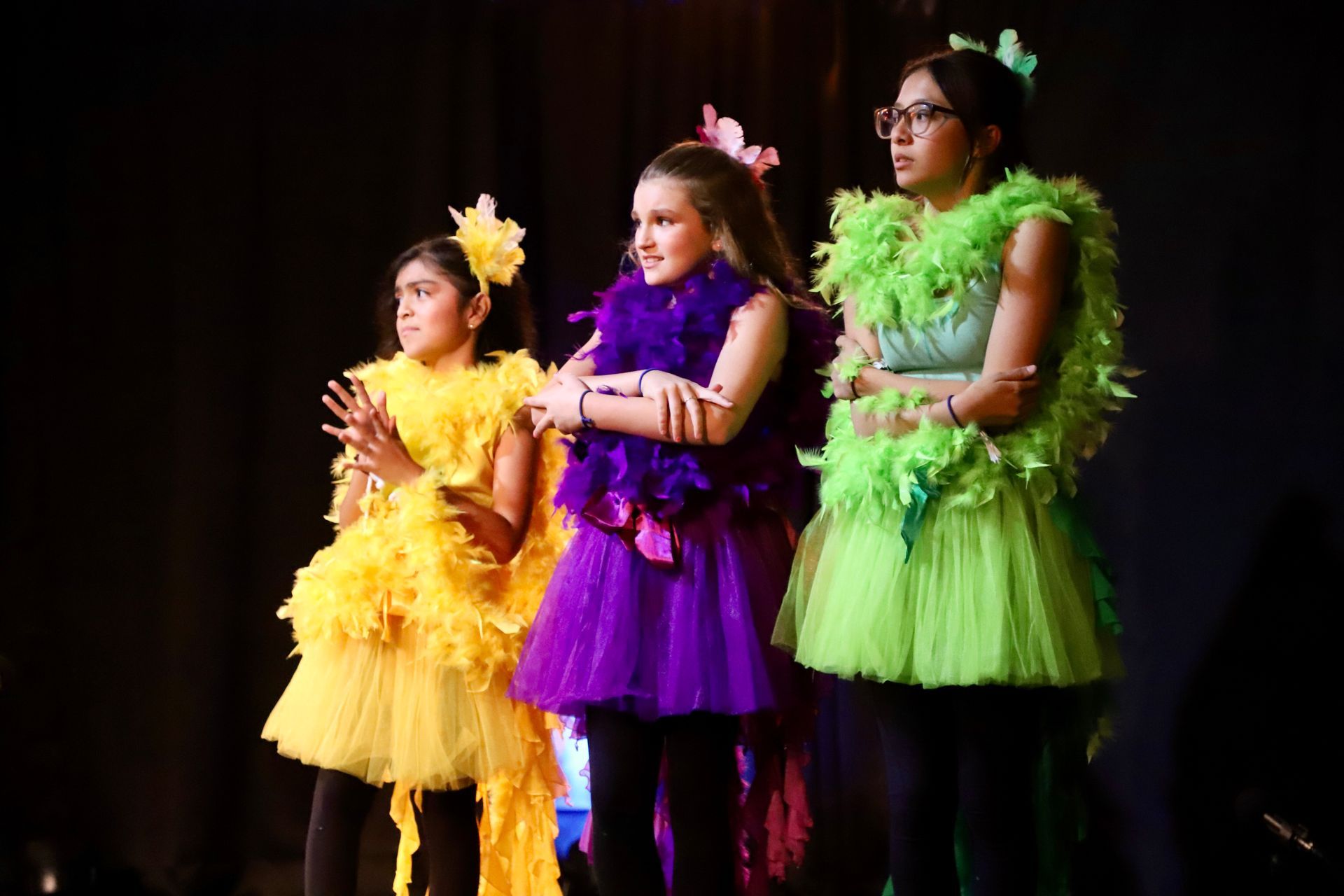 Three young girls are standing on a stage wearing colorful costumes.
